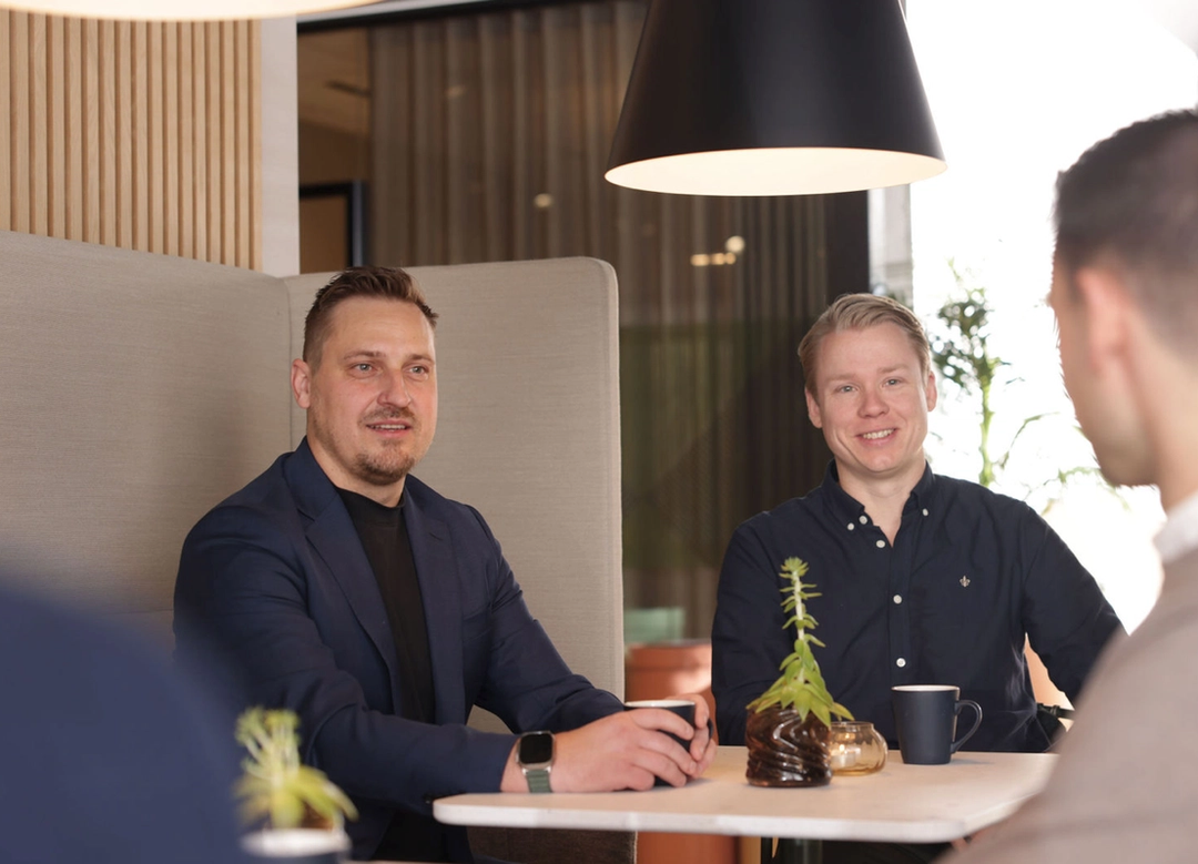 Tre ansatte rundt et bord nyter en kopp kaffe