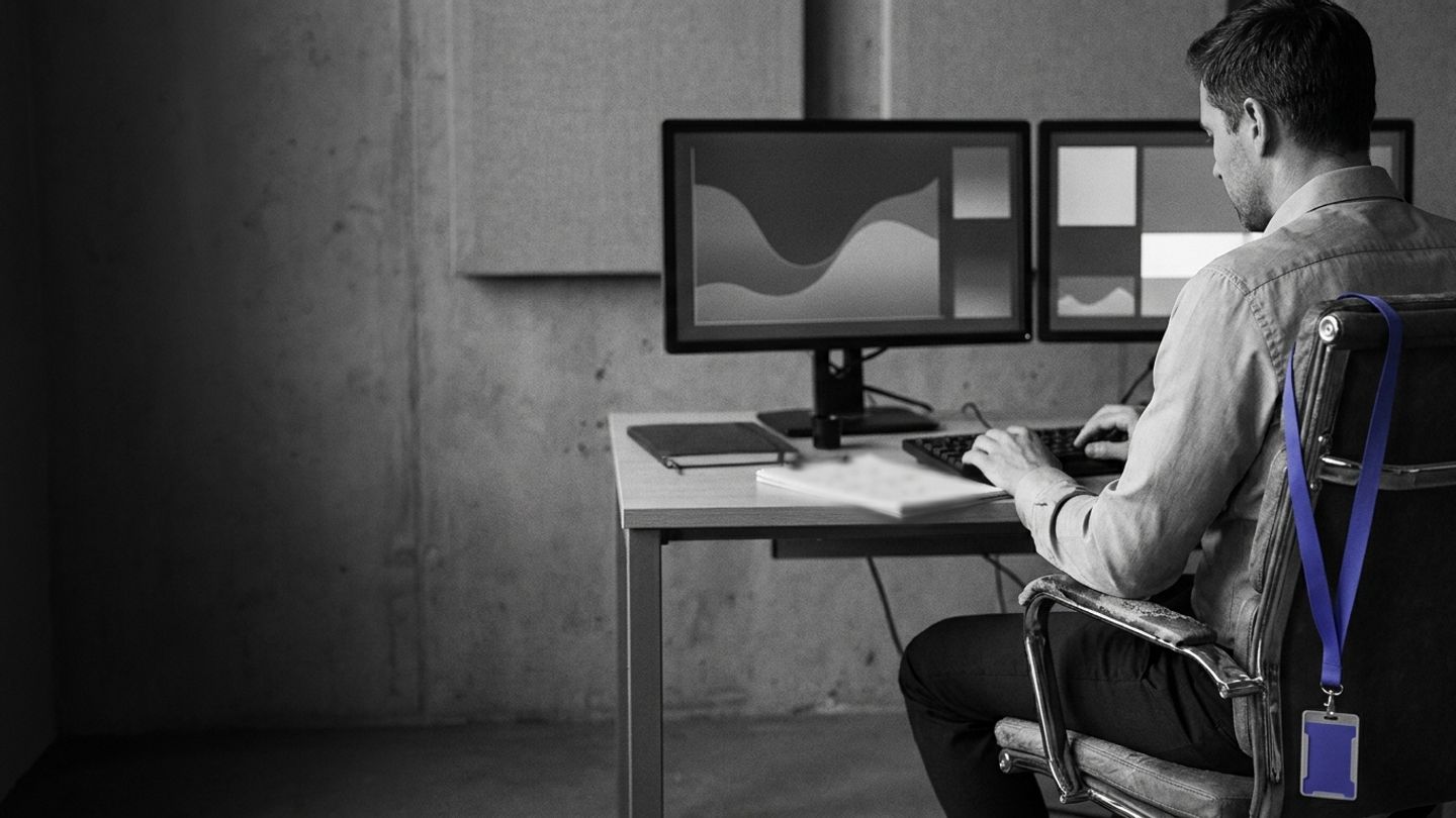 Professional in a control room watching monitors, monochrome with an indigo lanyard on the chair