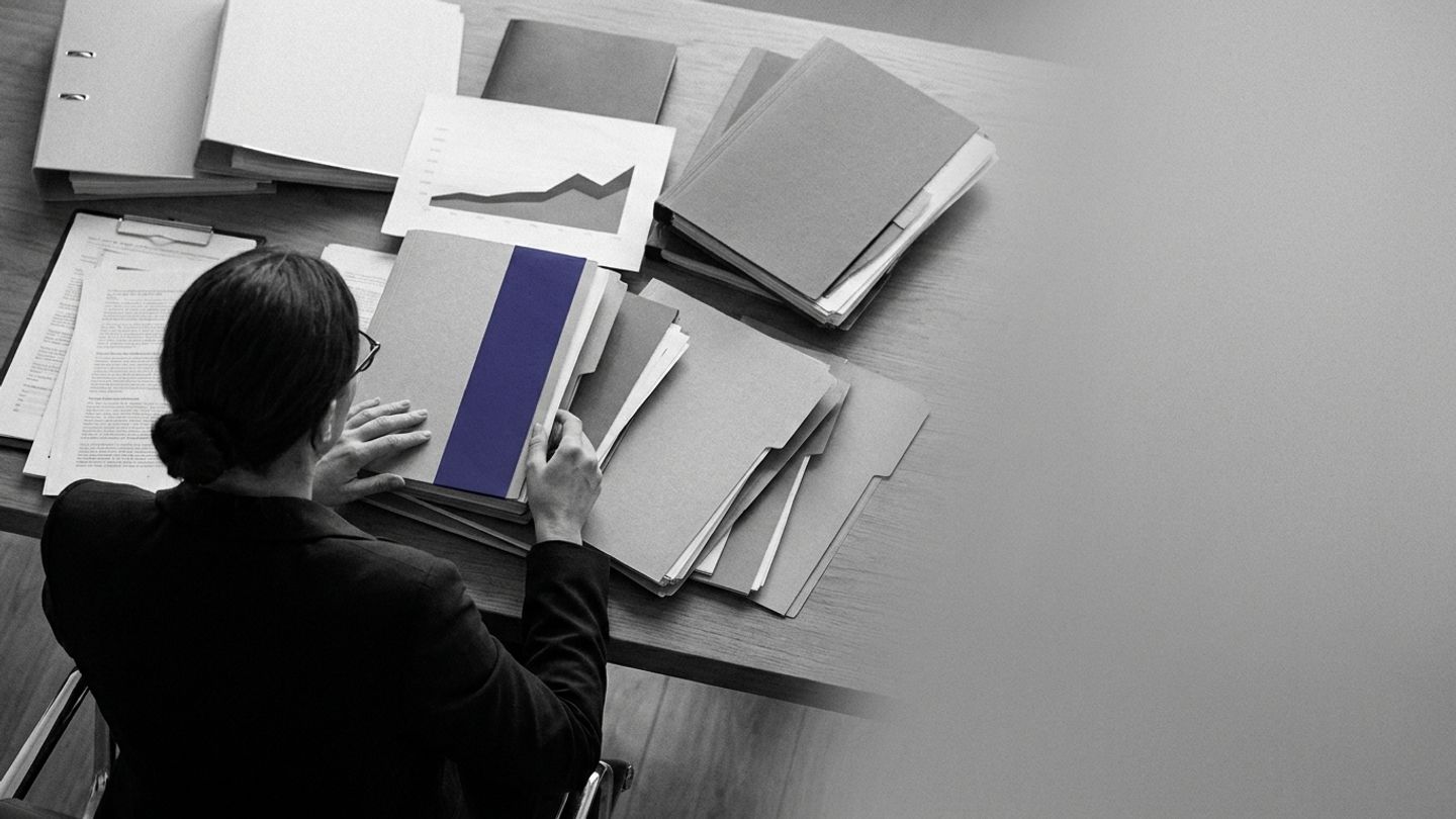Overhead view of a professional reviewing layered documents and binders, with a single indigo folder spine