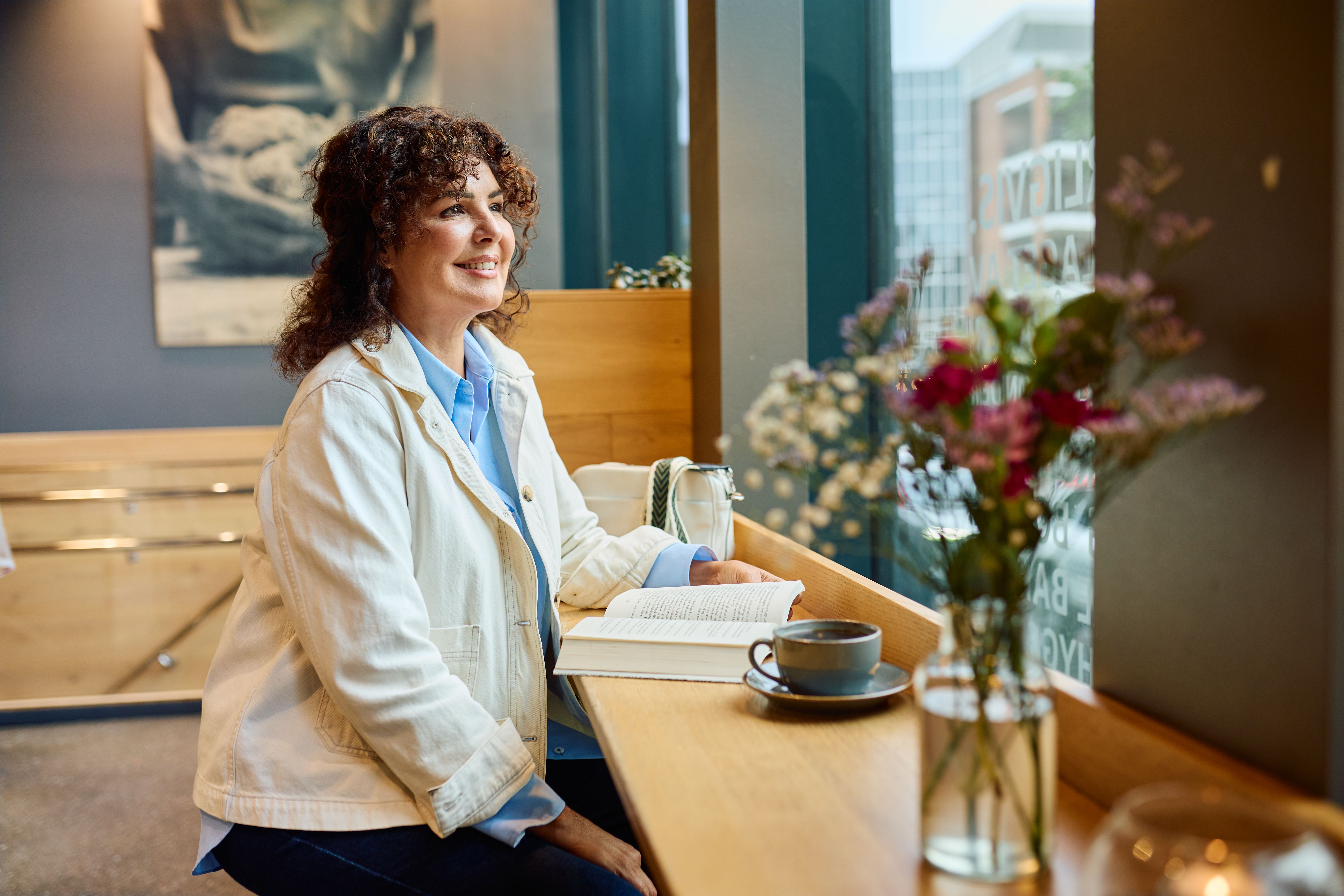 Kvinne som leser bok i vinduskarmen på en kafe.