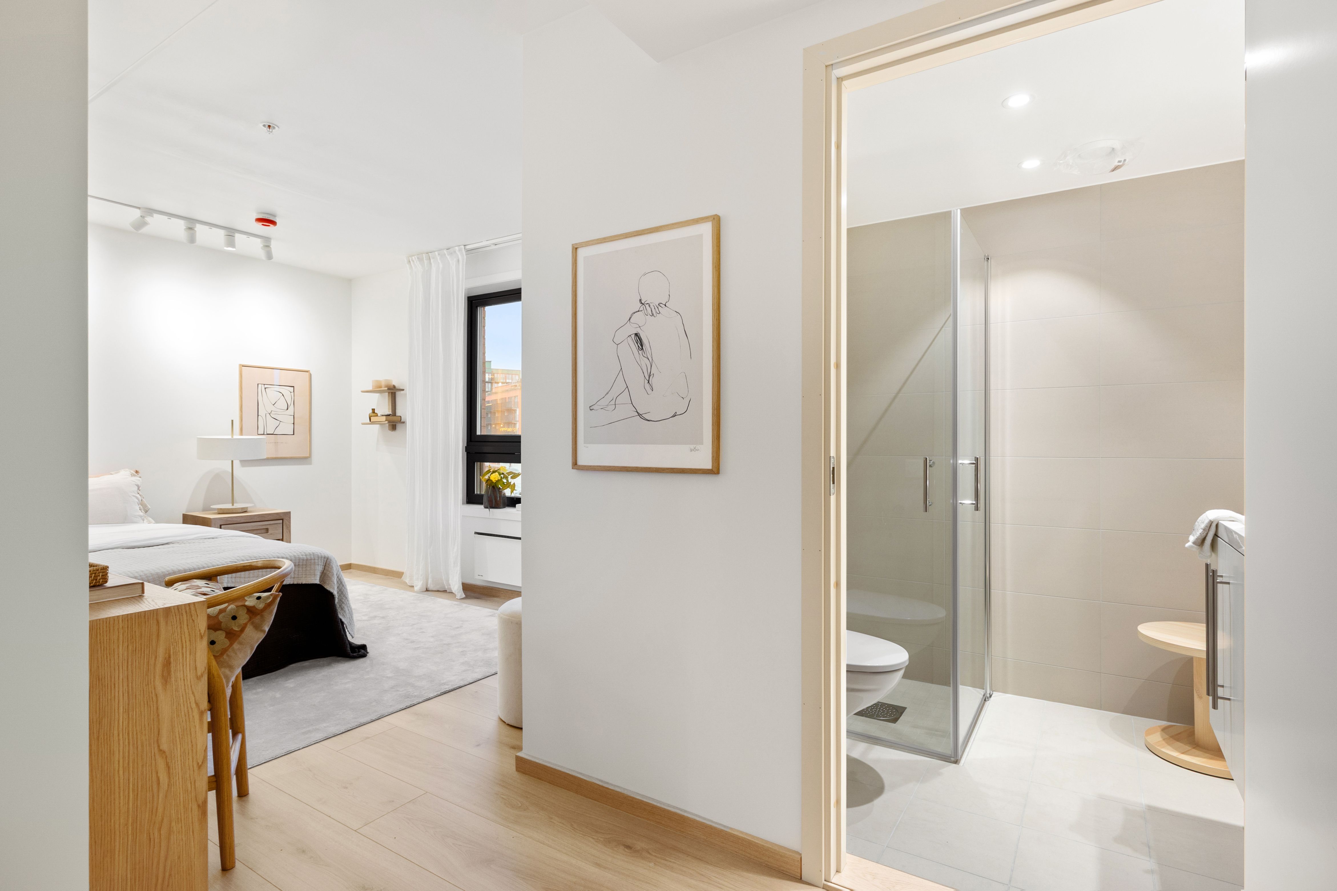 Rom med seng og skrivebord og åpen dør inn til bad