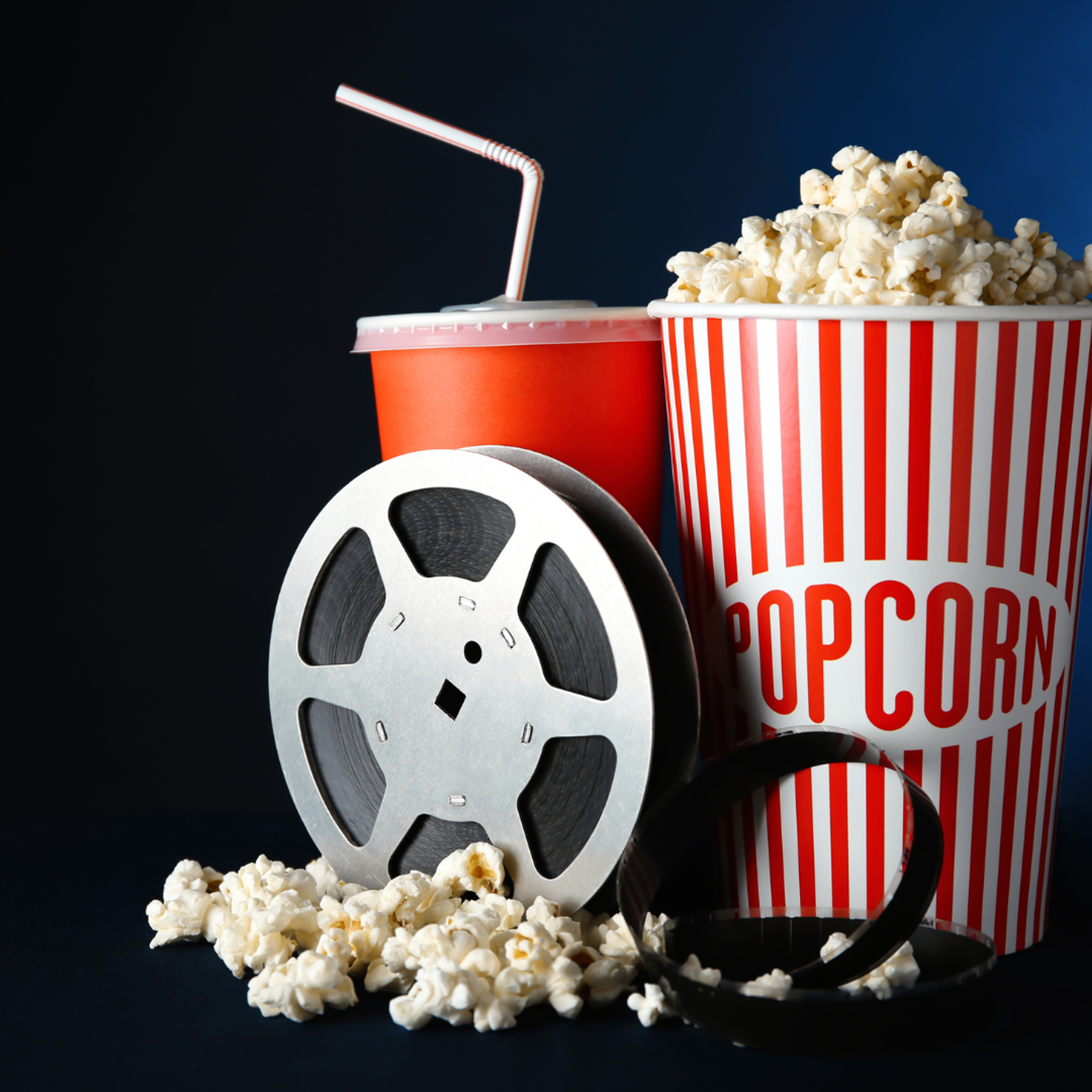 En stor bøtte med popcorn som står ved siden av et rødt beger med brus og filmrull