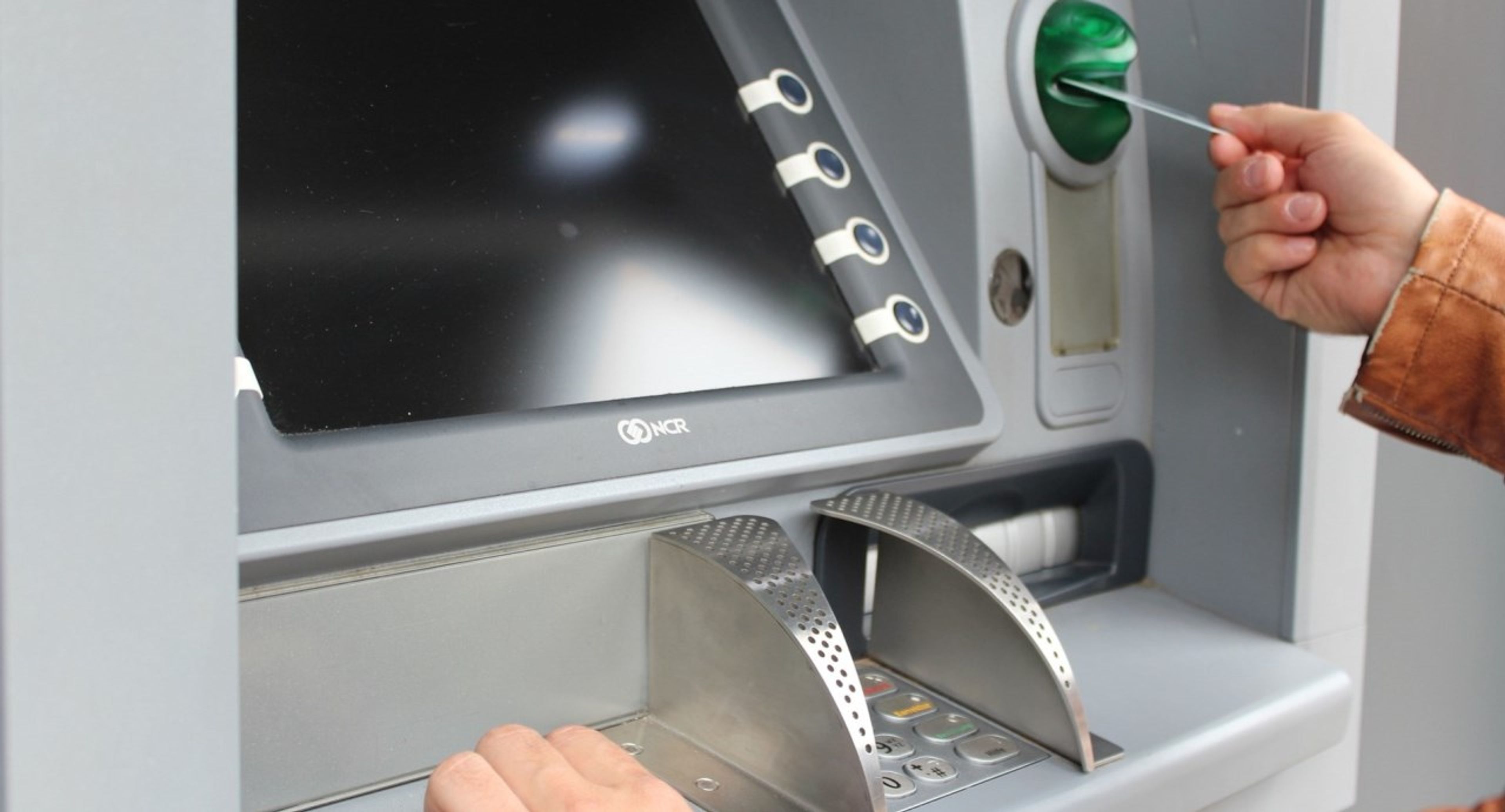 En person putter kortet sitt inn i minibanken. Foto.