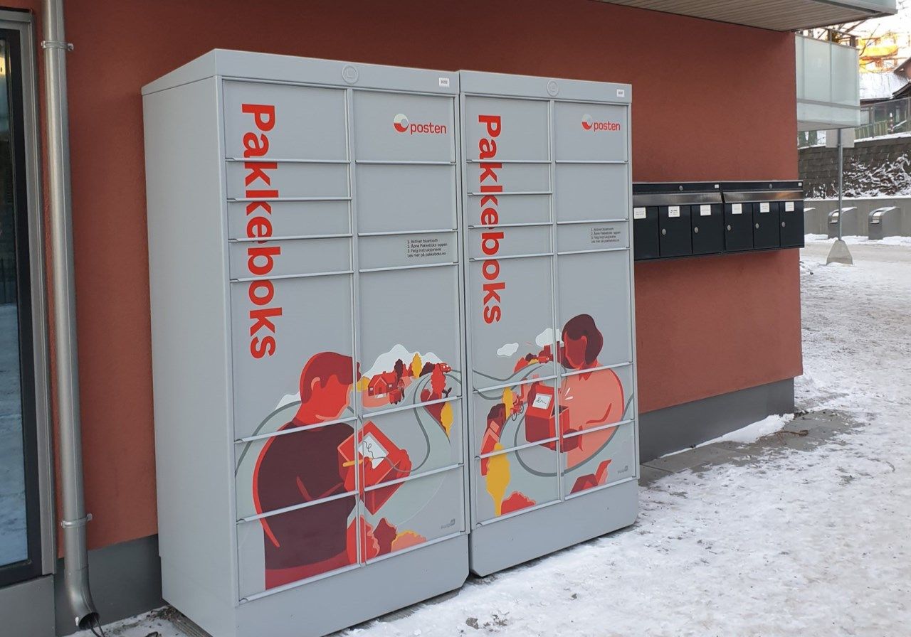 Foto av pakkebokser fra Posten utenfor en boligblokk.