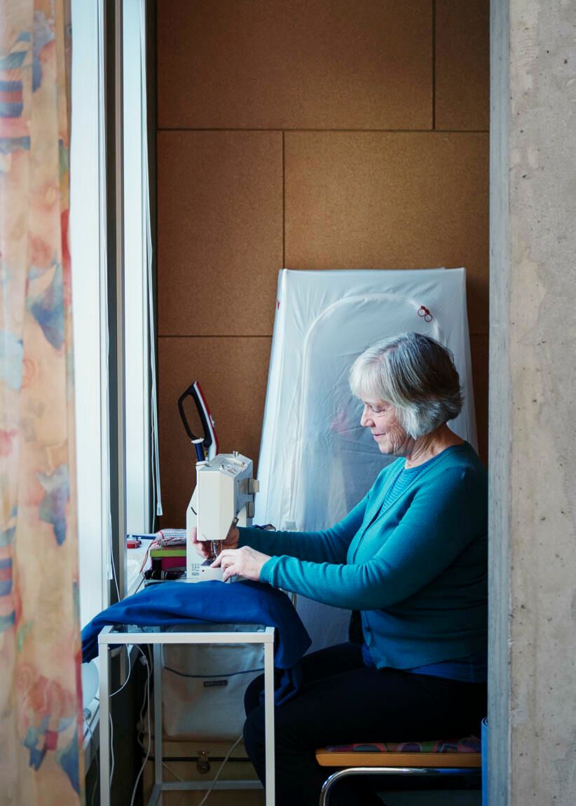 Beboer i OBOS Living Lab, Else Bakkehaug, sitter foran en symaskin og syr i blått stoff