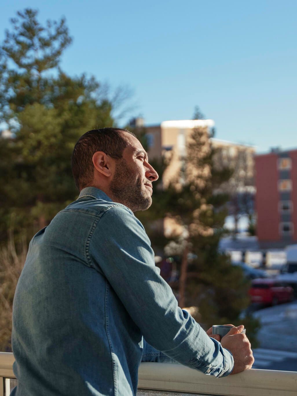 En mann står på verandaen og titterutover. Han har en kopp kaffe i hånda.