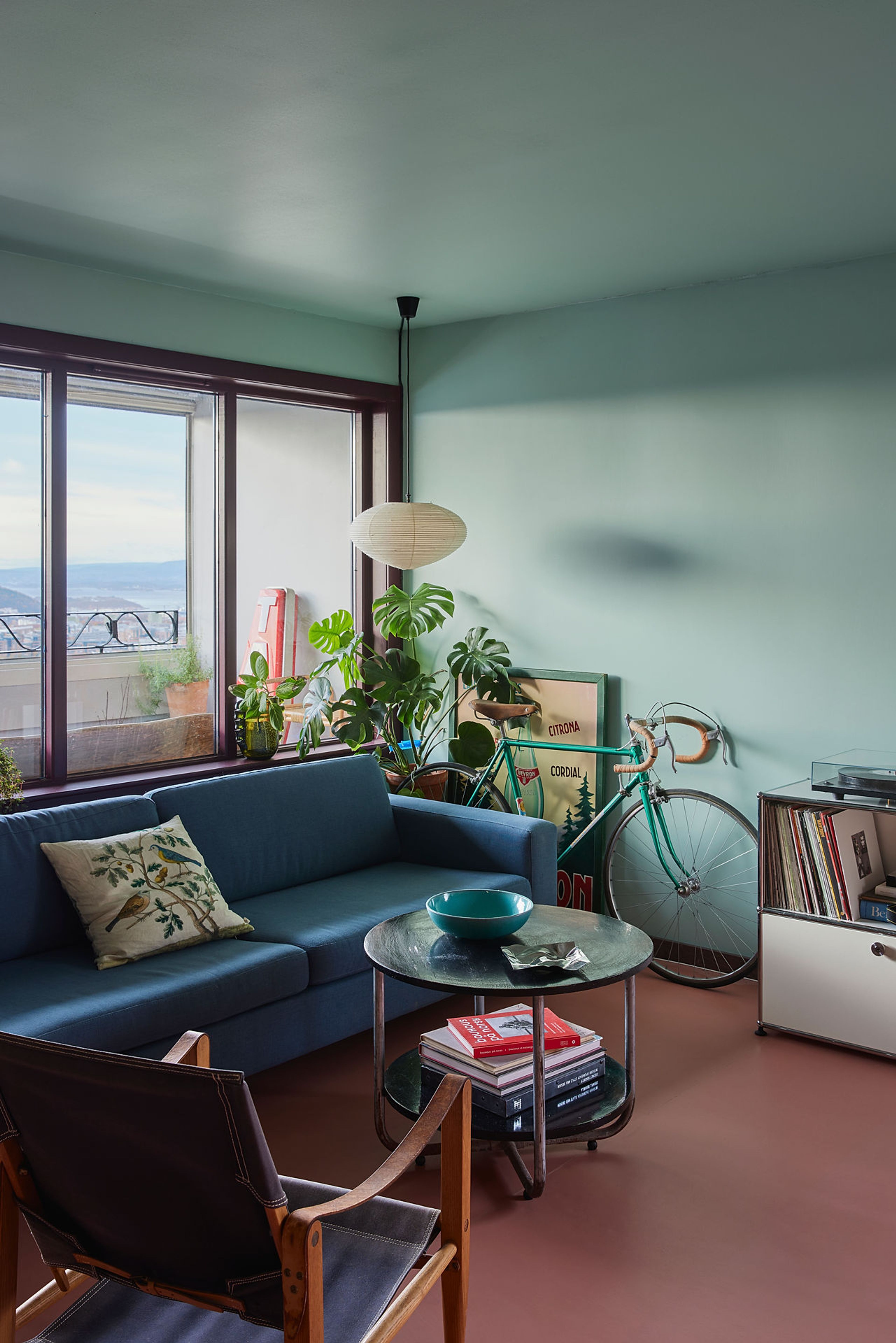 Stua er godt møblert med en blå sofa, en stol, et sofabord og i hjørnet står det en retro sykkel.