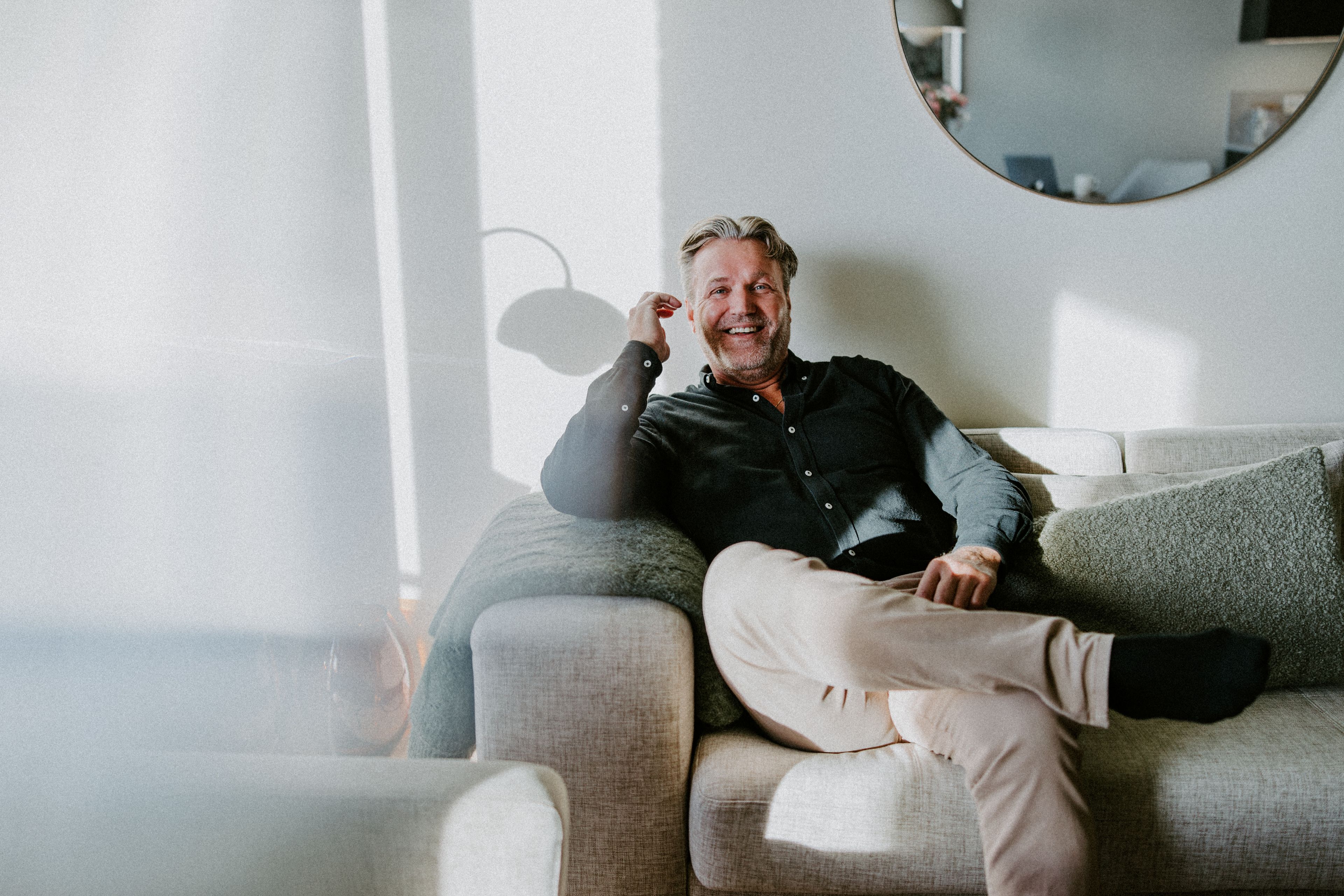 Even Aase sitter tilbakelent i sofaen i stua si og ler, med sollys inn gjennom vinduet.