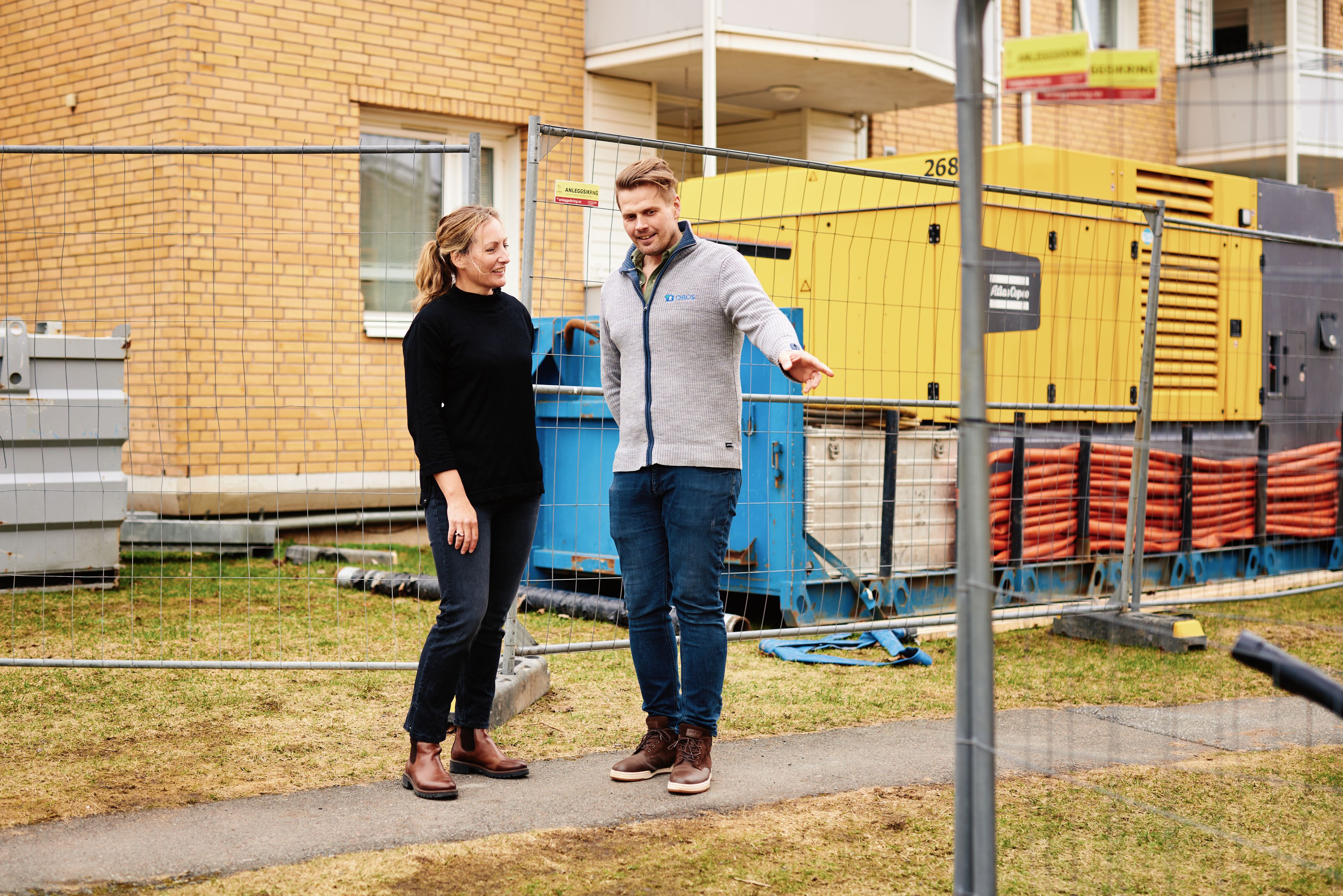 To personer står utenfor en boligblokk som er under rehabilitering