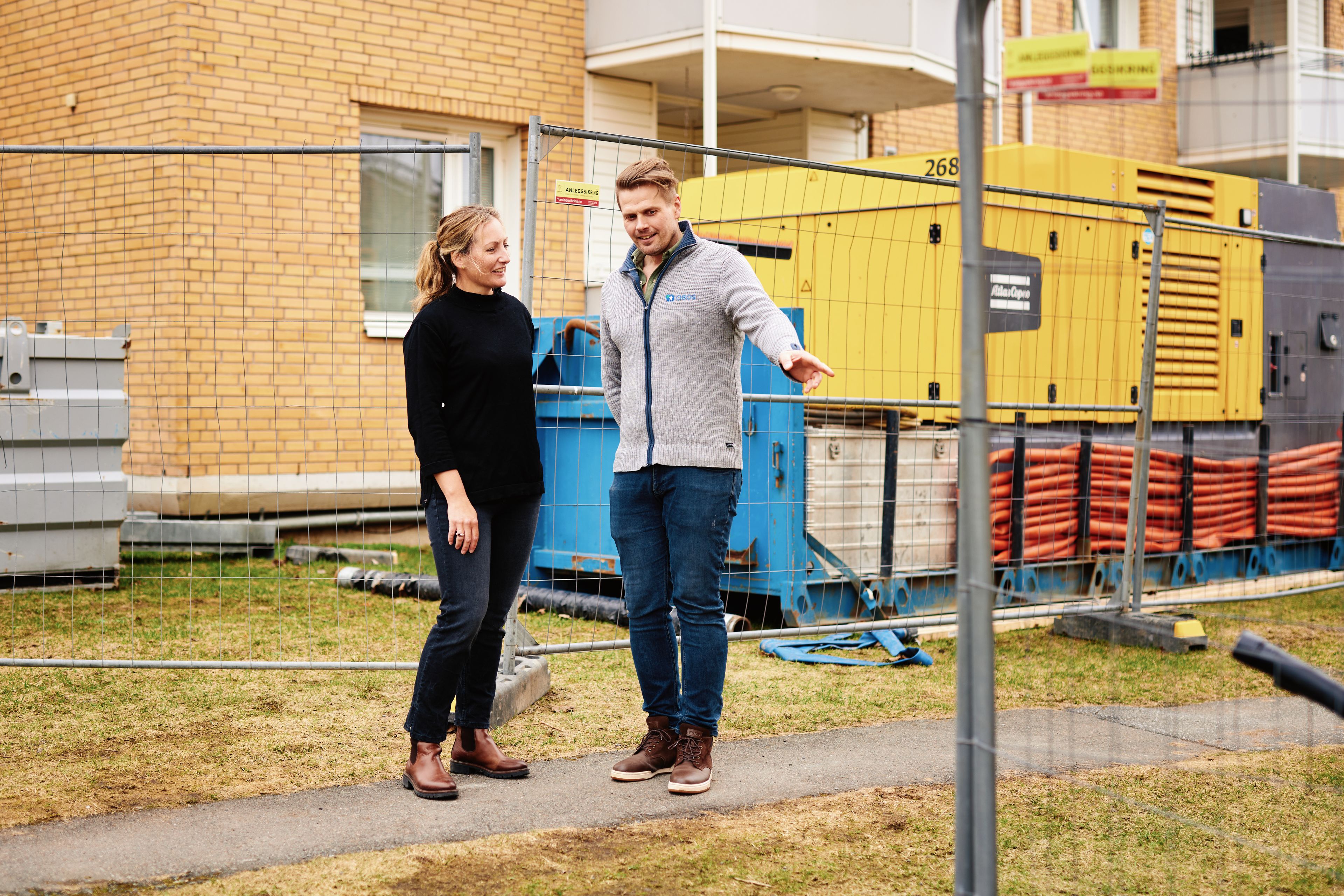 To personer står utenfor en boligblokk som er under rehabilitering