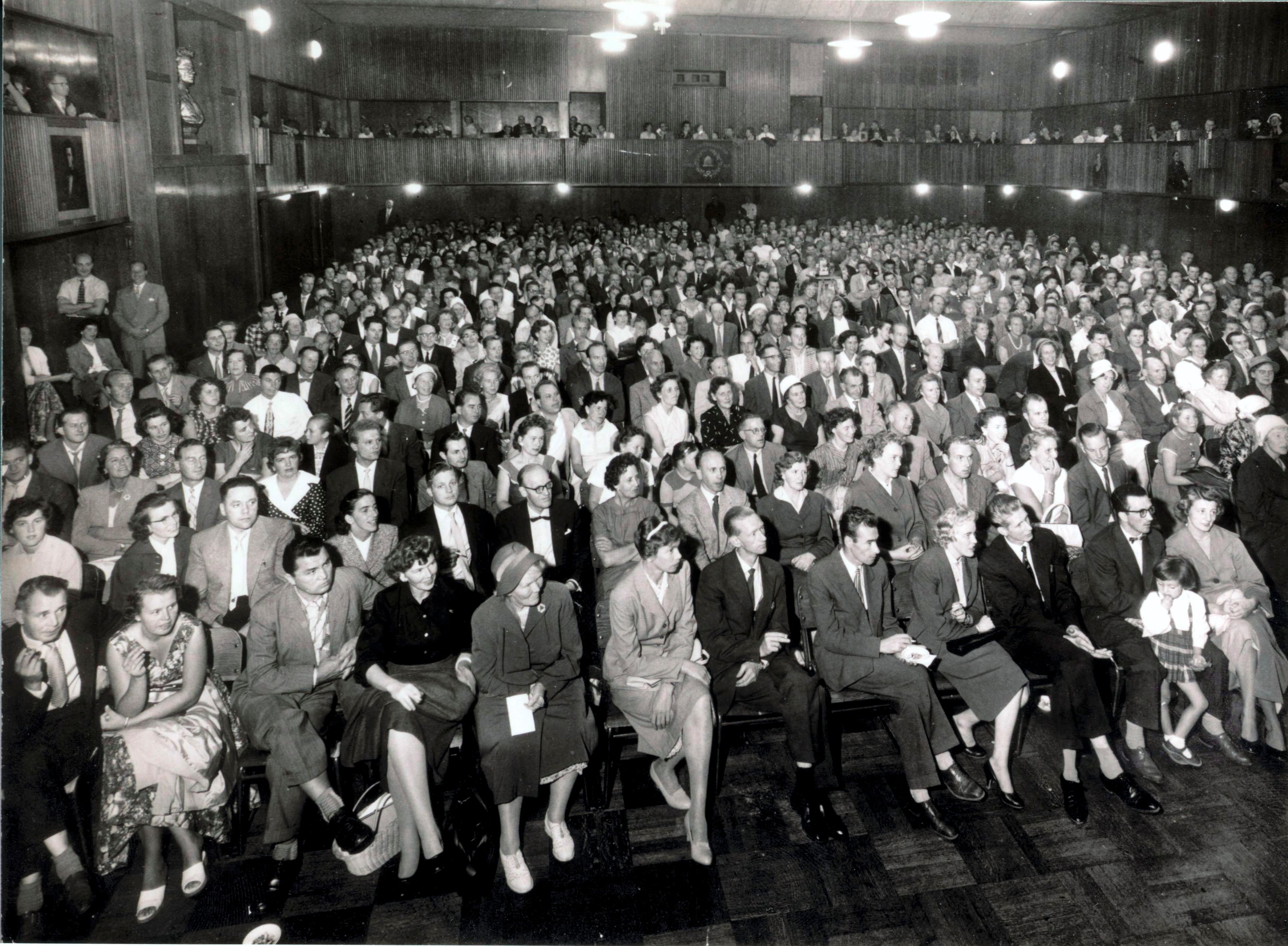 Et gammelt bilde av en sal full av forventningsfulle mennesker som håper at de får bolig. 