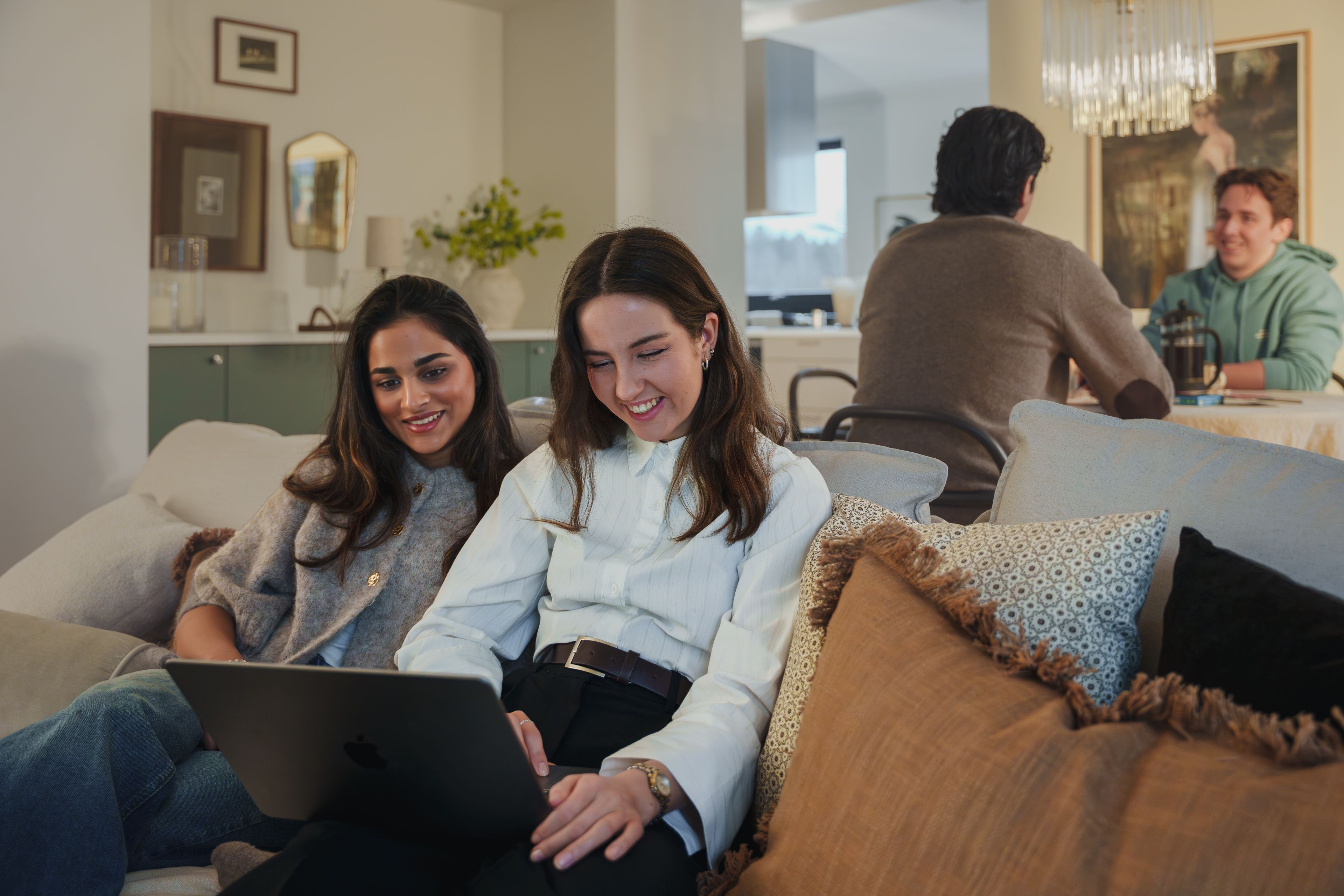 To unge kvinner sitter i en sofa og jobber over pc-en