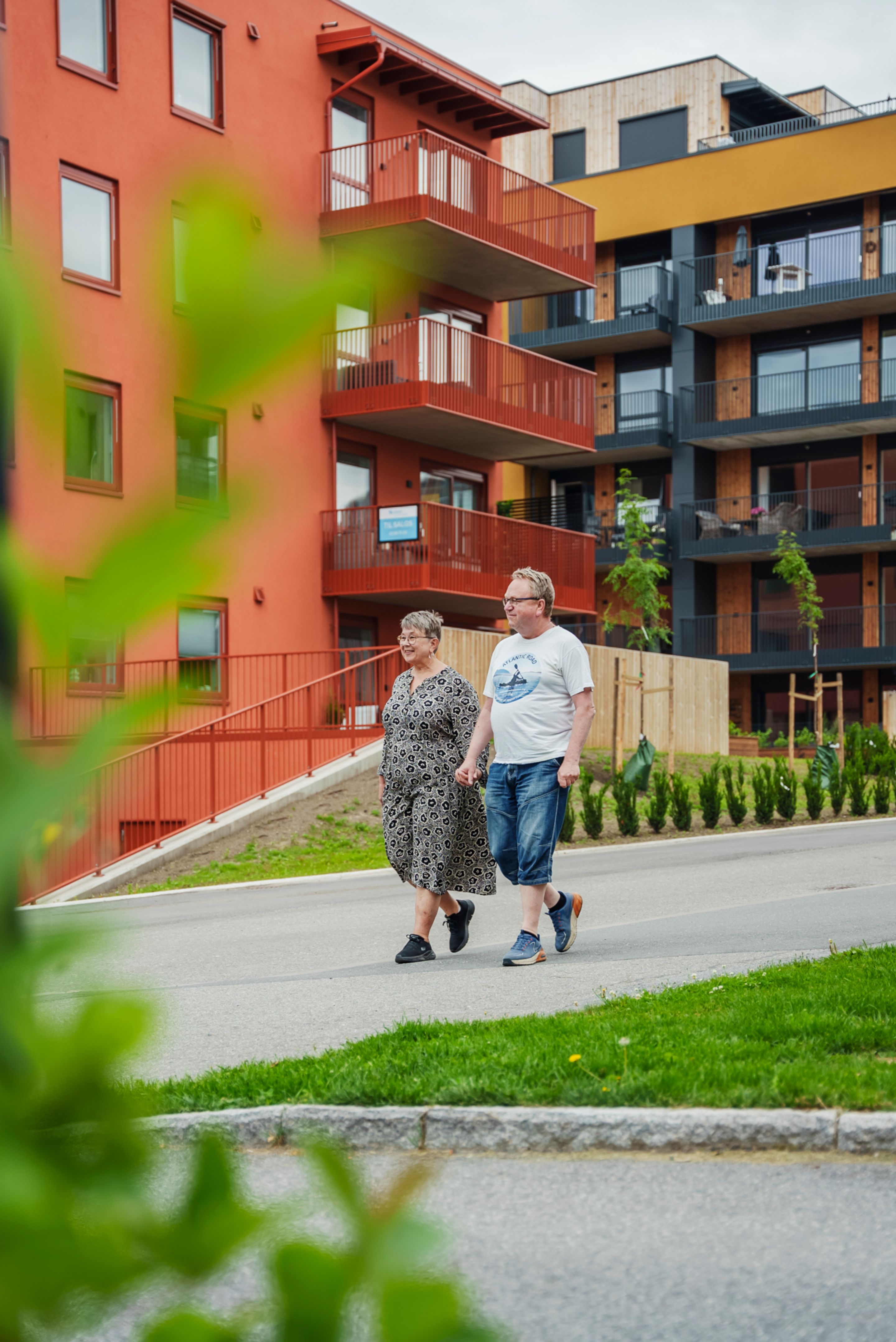 Bilde av Ingrid Raasholm og Rune Gihlemoen som går på en gangvei foran et rødt og gult leilighetsbygg