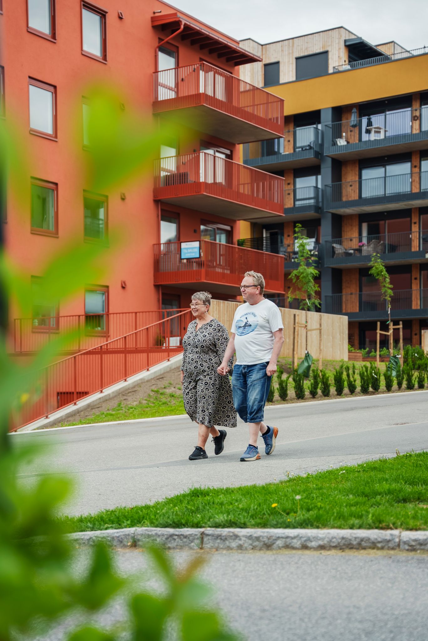 Bilde av Ingrid Raasholm og Rune Gihlemoen som går på en gangvei foran et rødt og gult leilighetsbygg