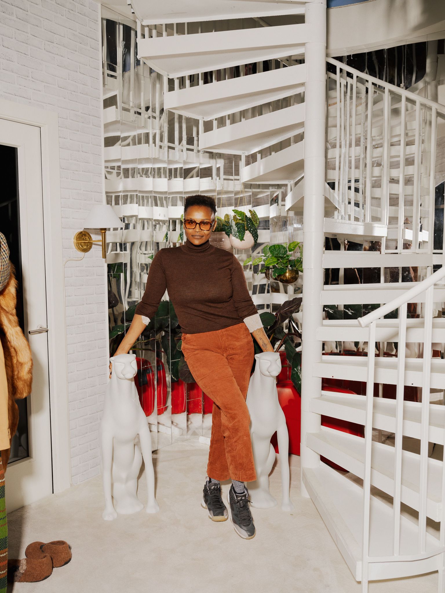 Jae Nyamburah står under en hvit virveltrapp og lener seg mot to skulpturer.