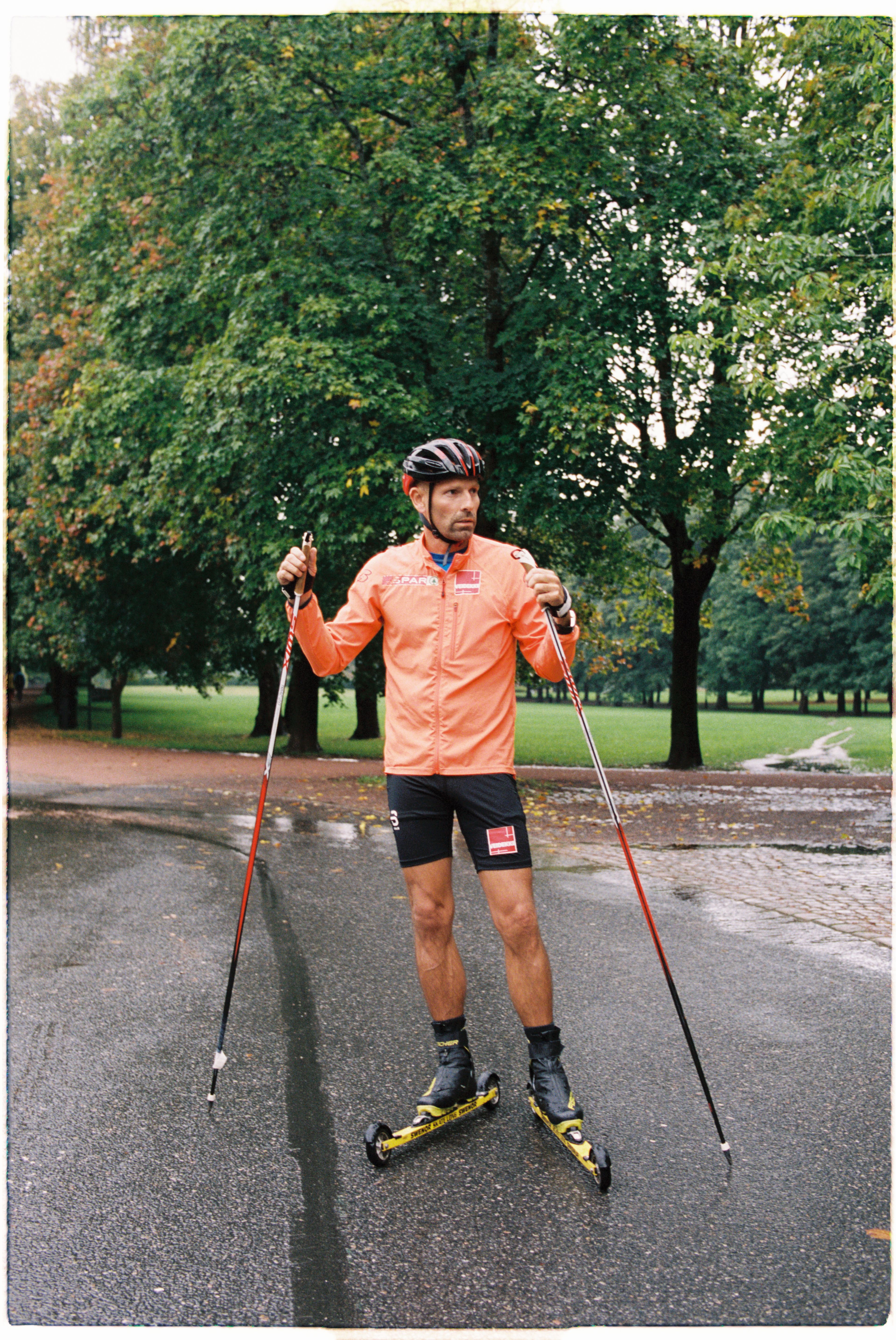Jonas Kinge Bergland har på seg oransje treningstøy, har en hjelm på hodet og rulleski på beina.