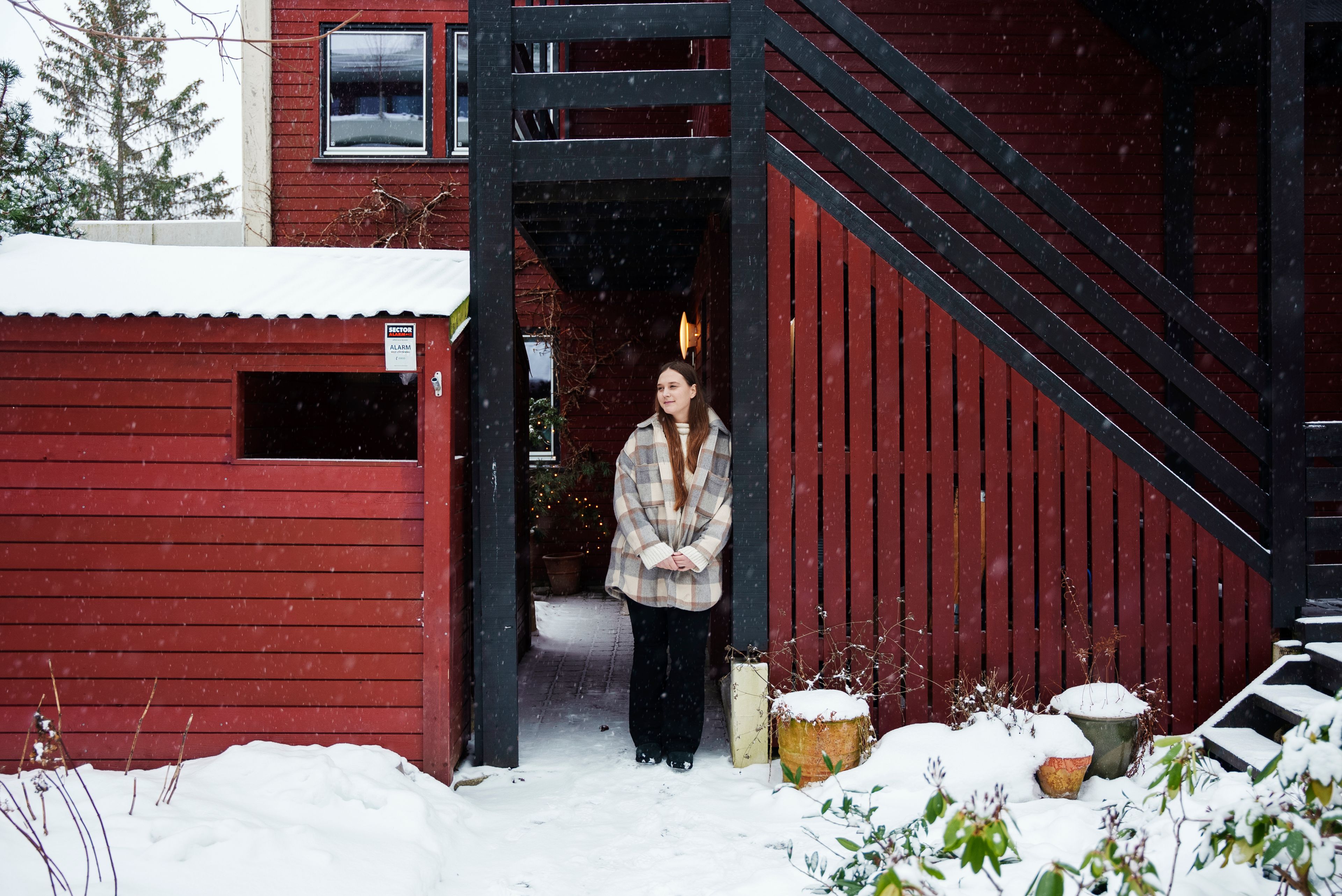 Kristine Istad som står i snøværet, lent mot det røde inngangspartiet til boligen sin