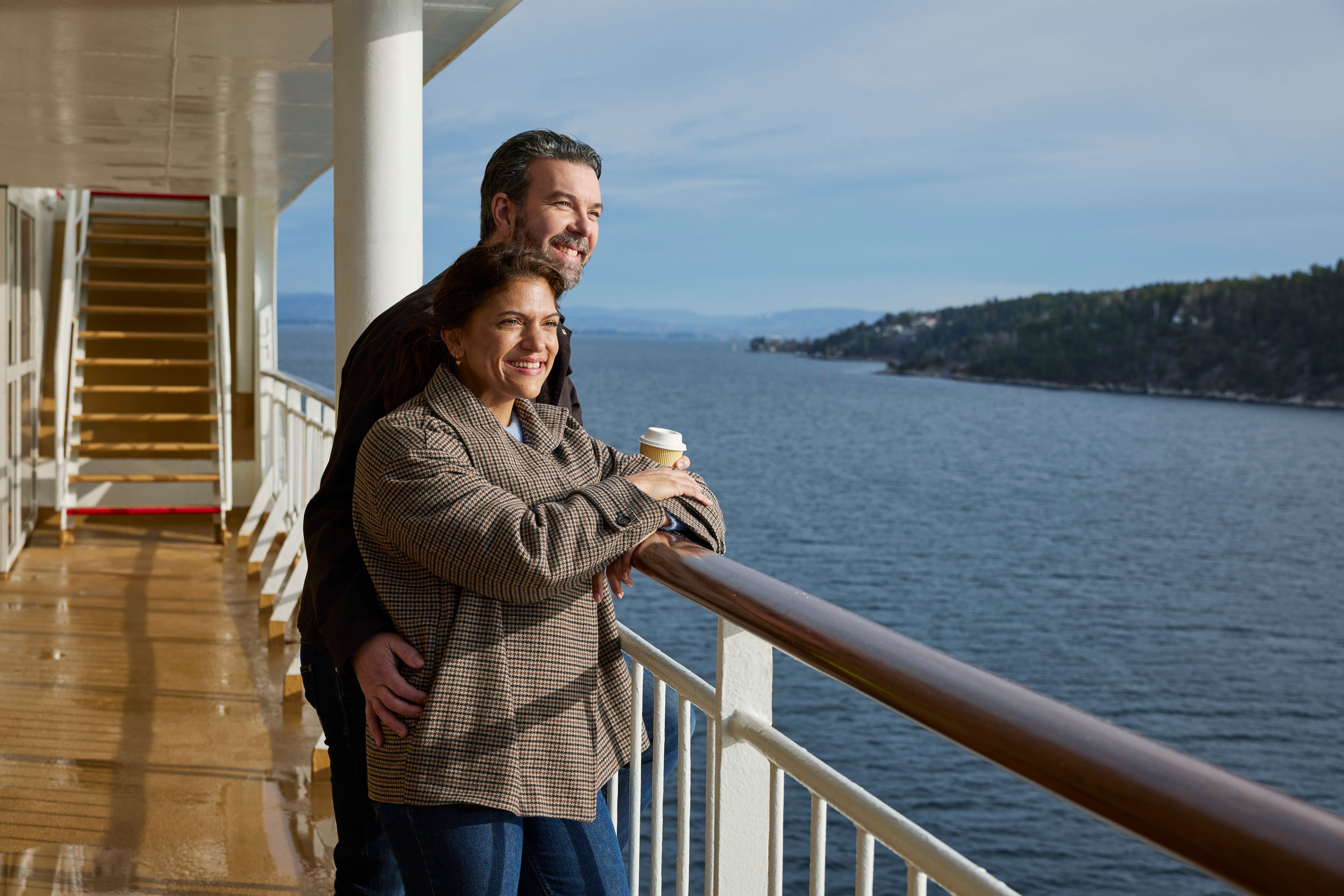 Et par står ute på dekk på et cruiseskip og ser ut over fjorden.
