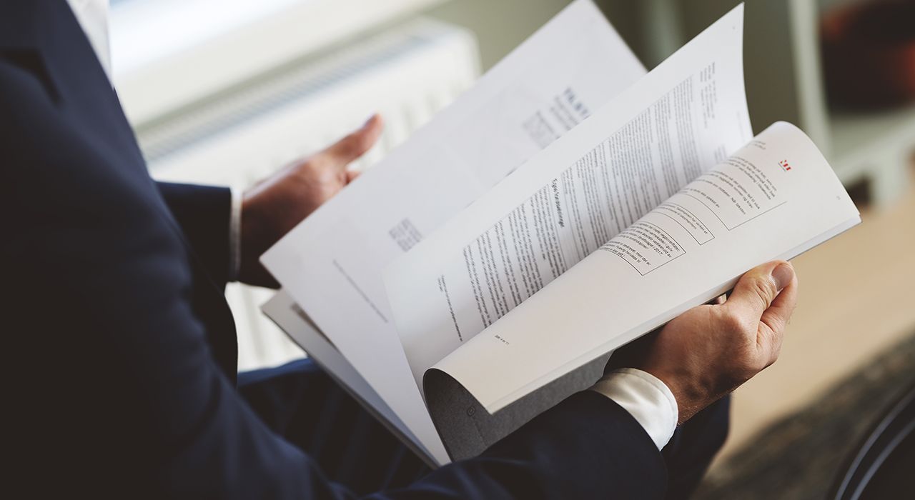 Nærbilde av mann i dress som blar i et prospekt.