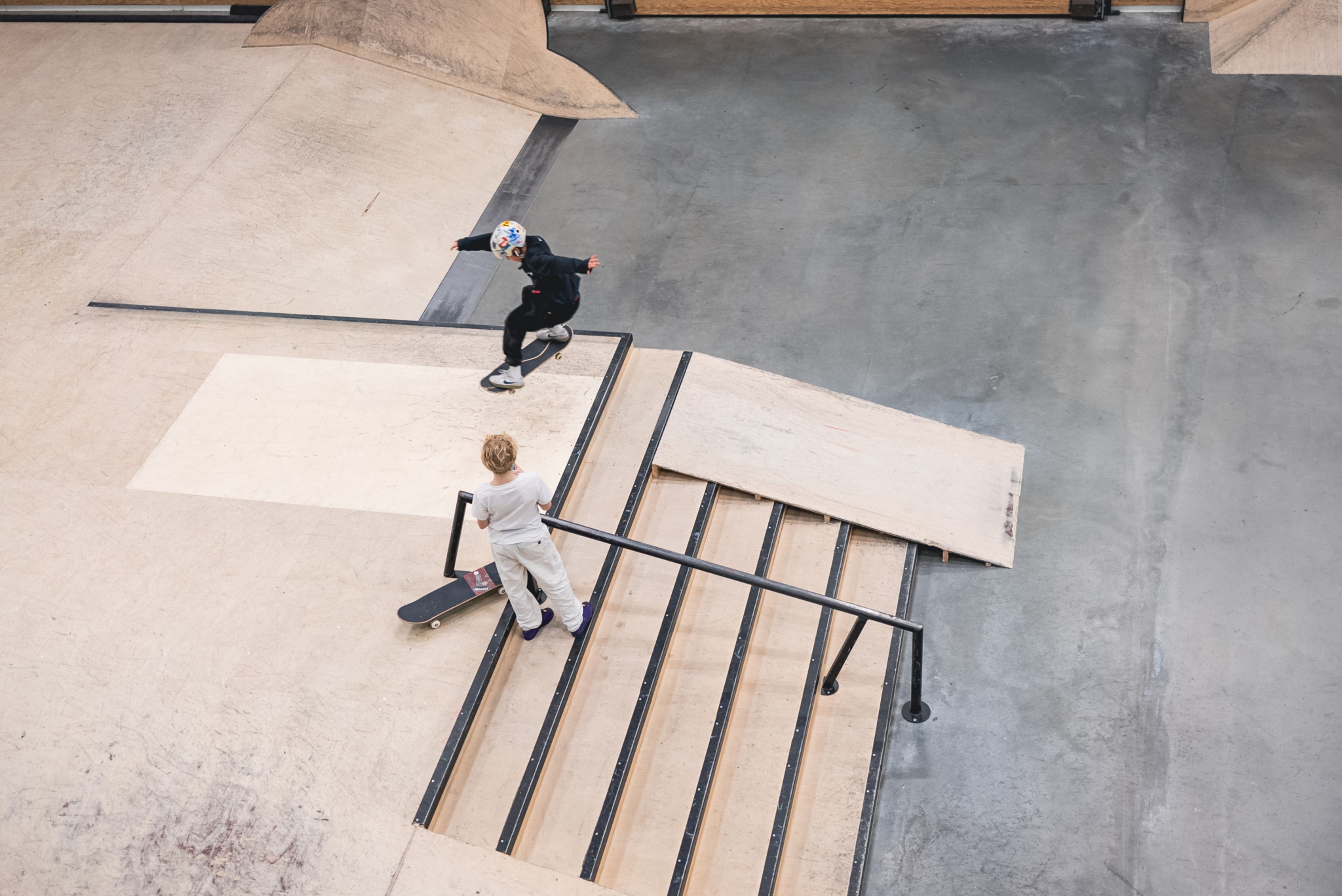 Foto fra fugleperspektiv av skatehallen hvor to gutter øver på skatetriks over et hinder