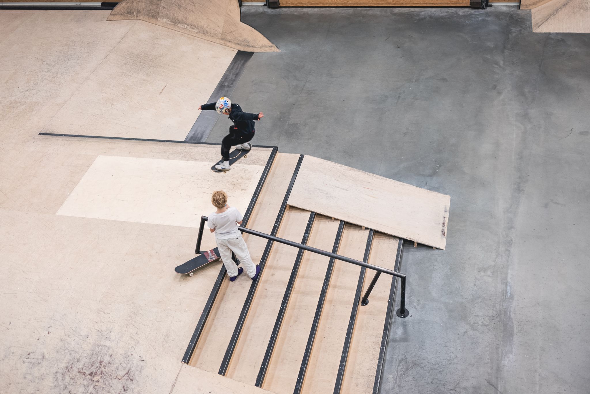 Foto fra fugleperspektiv av skatehallen hvor to gutter øver på skatetriks over et hinder