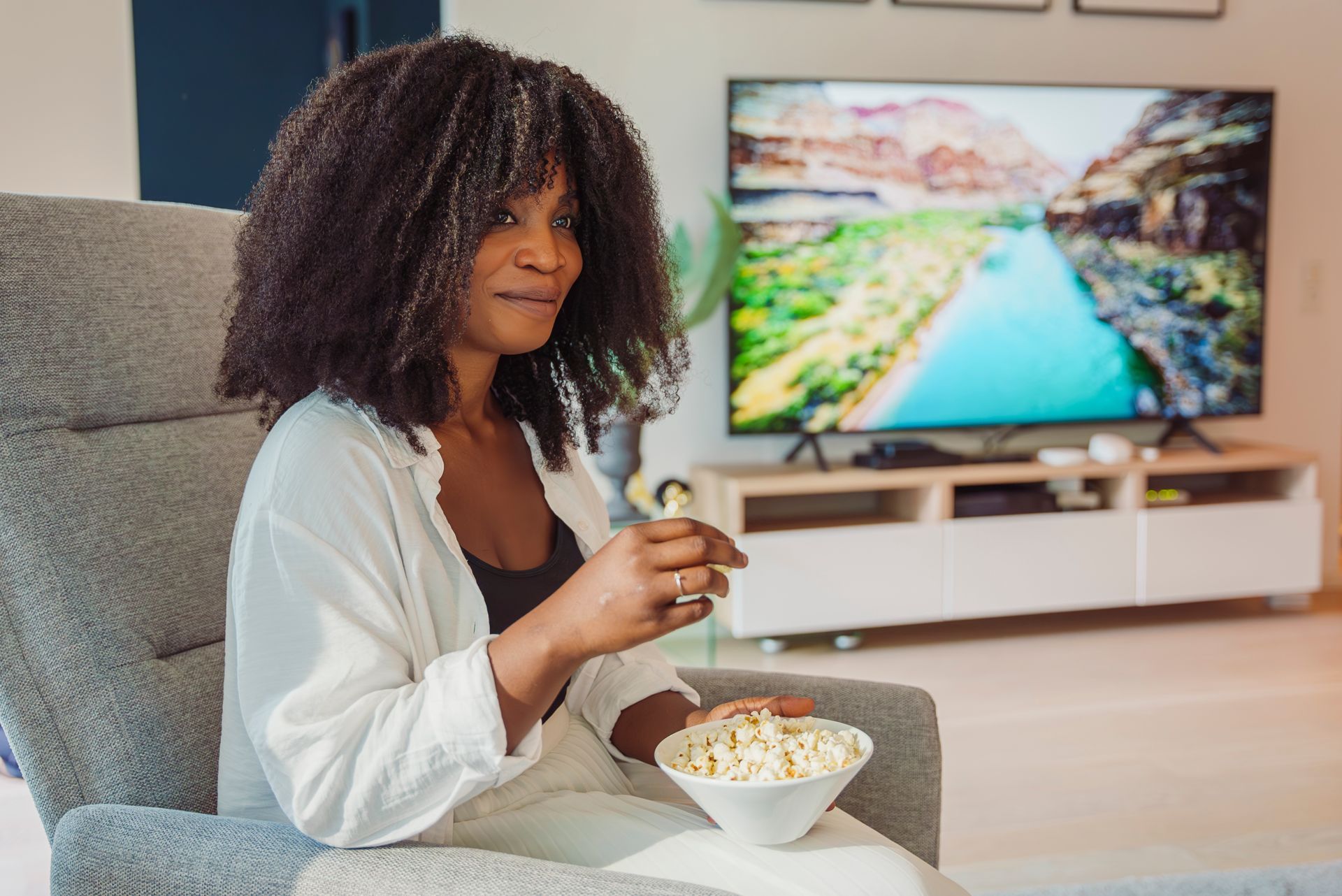 Kvinne sitter i en stol og ser på TV mens hun spiser popcorn