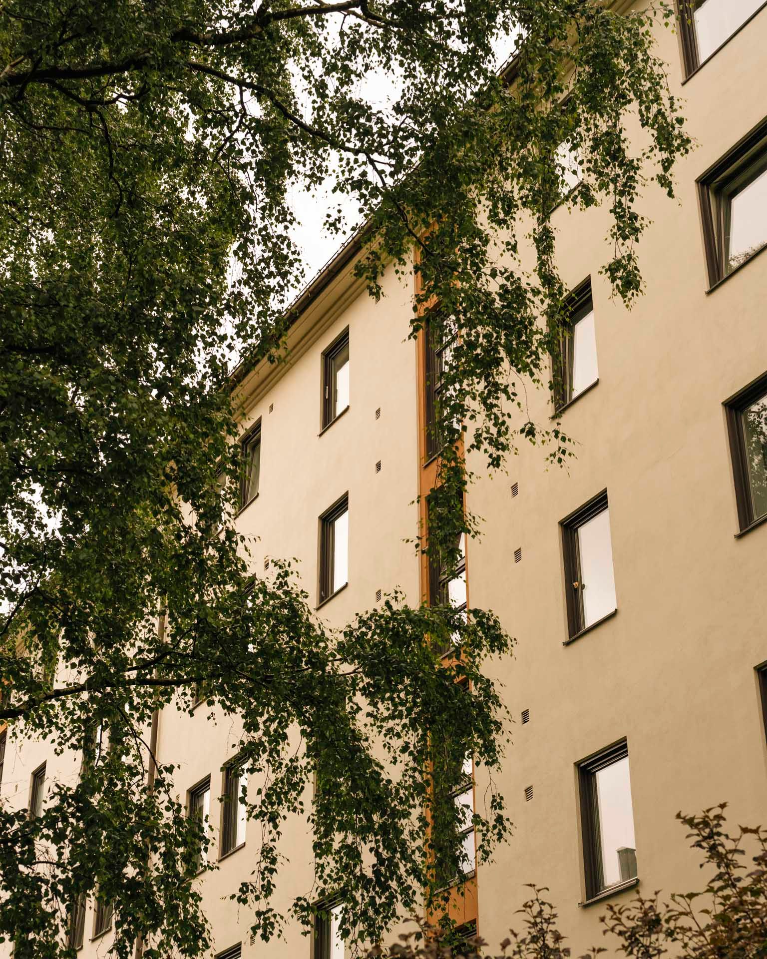 Fasade av boligbygning ved Gjøvikgata borettslag med beige vegger, store vinduer og grønt klatrevegetasjon som dekker deler av veggen.