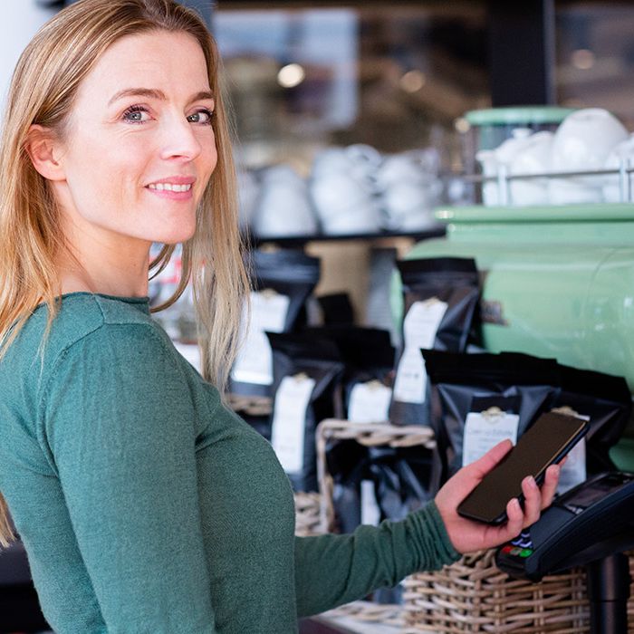 Dame i en kaffebar som betaler med bankkort på mobilen.