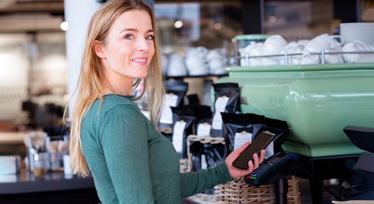 Dame i en kaffebar som betaler med bankkort på mobilen.