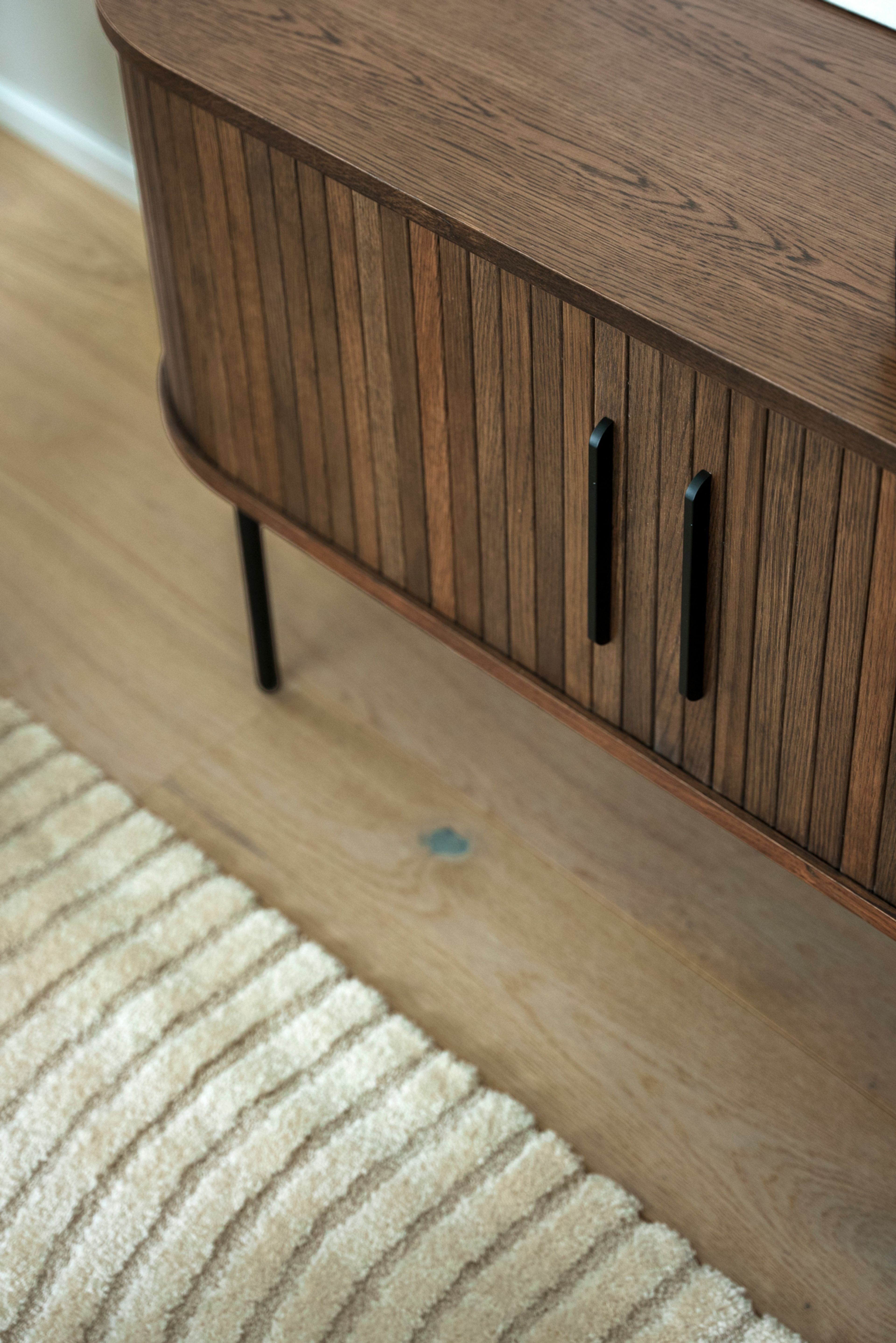 Nærbilde av en tv-benk i valnøtt og et lyst, organisk teppe i MIDT.