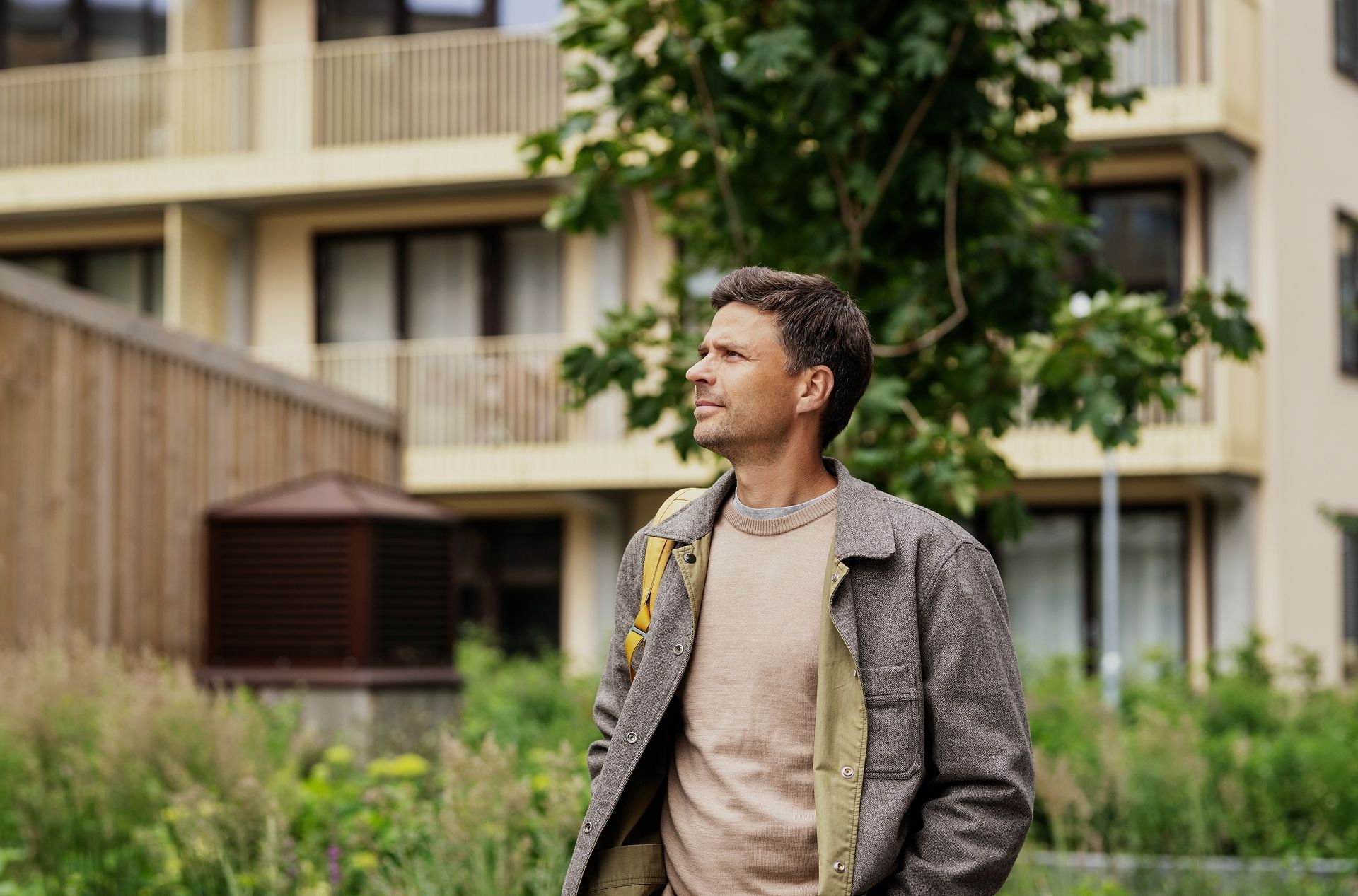 Mann står utenfor en boligblokk og ser opp mot fasaden.
