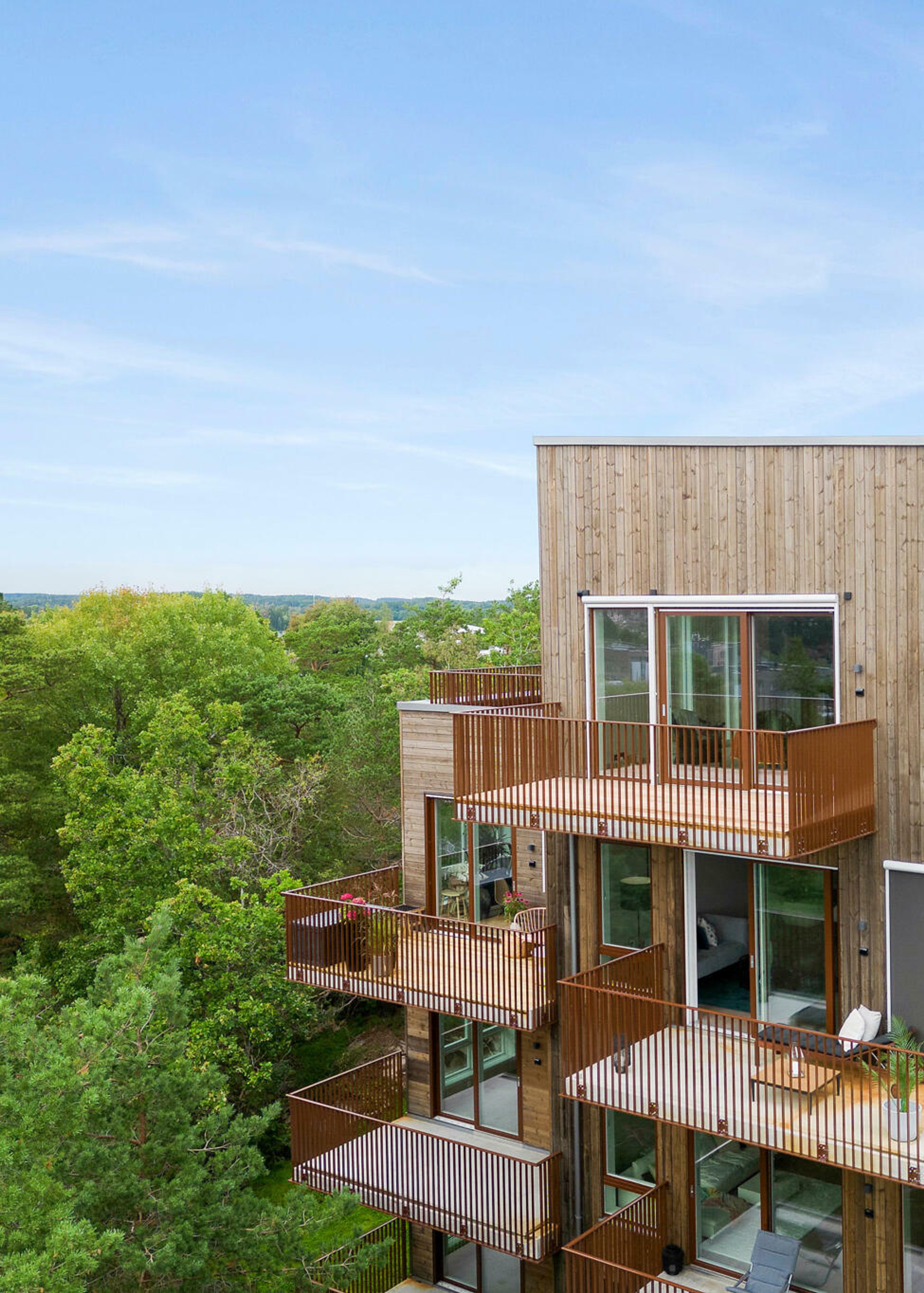 Fasaden og balkonger med grønne trær om sommeren.