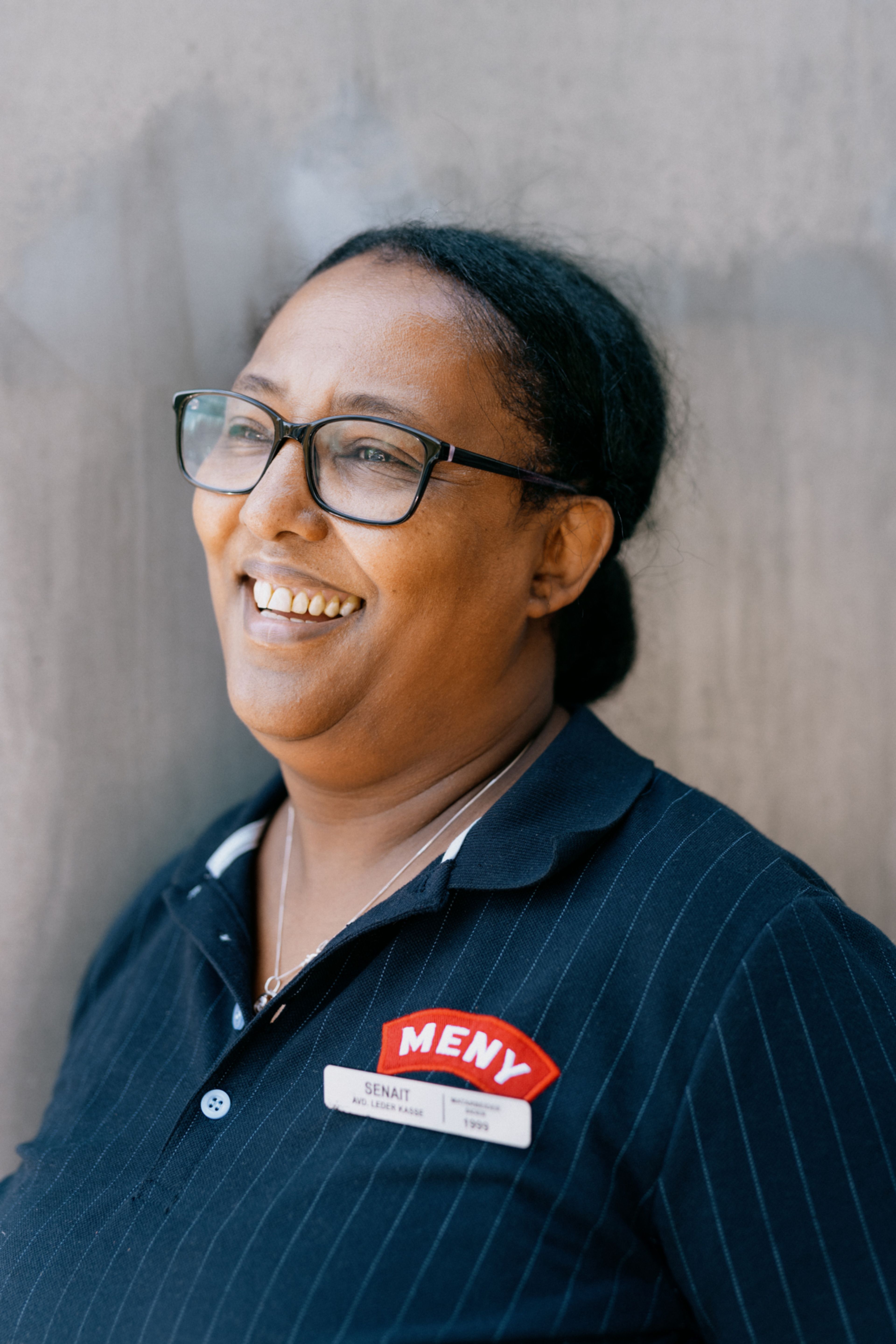 Senait smiler og ser mot venstre, og har på seg t-skjorte med Meny-logo og navneskilt.