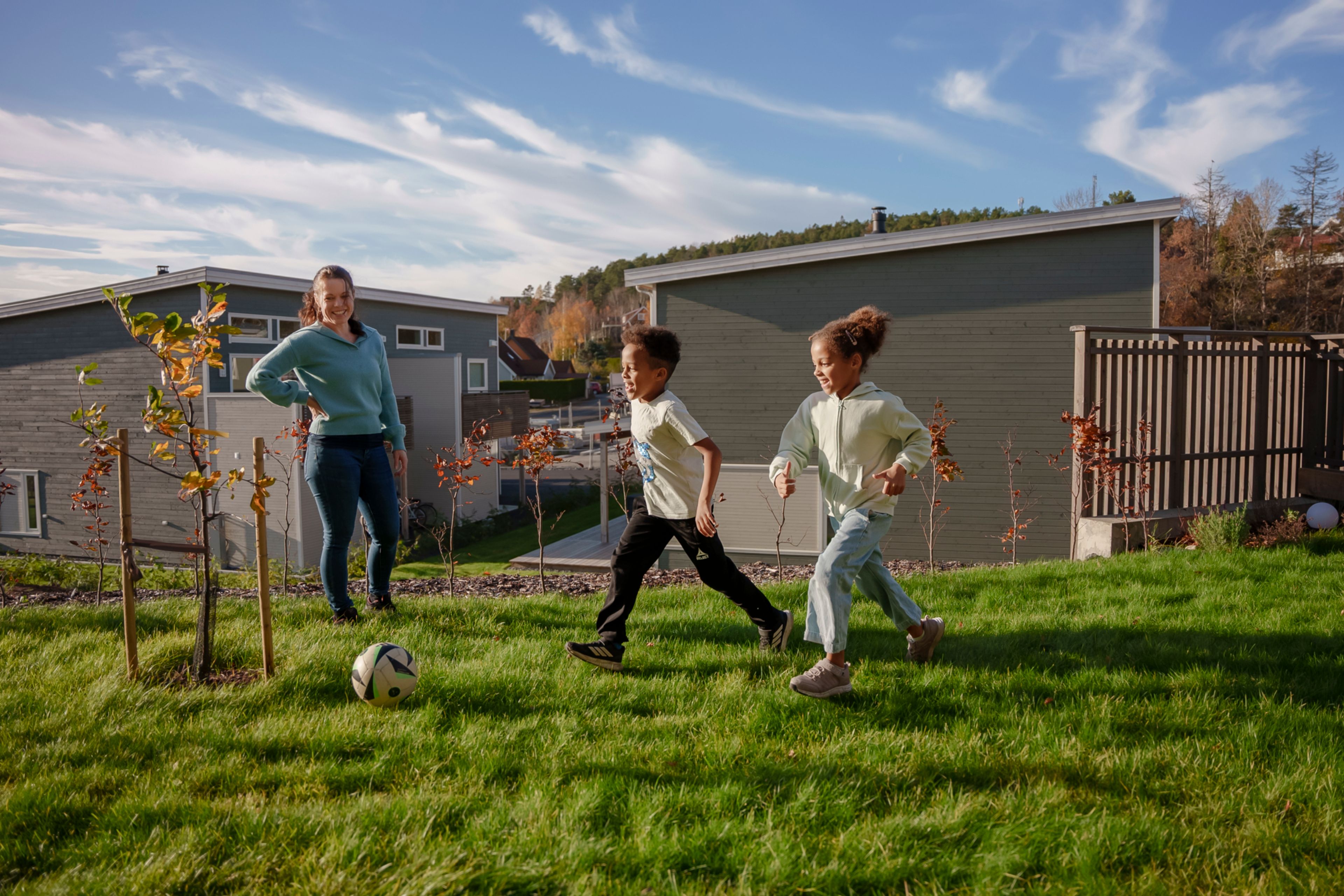 Eirin står og ser på mens barna leker i hagen og spiller fotball i kveldssolen.