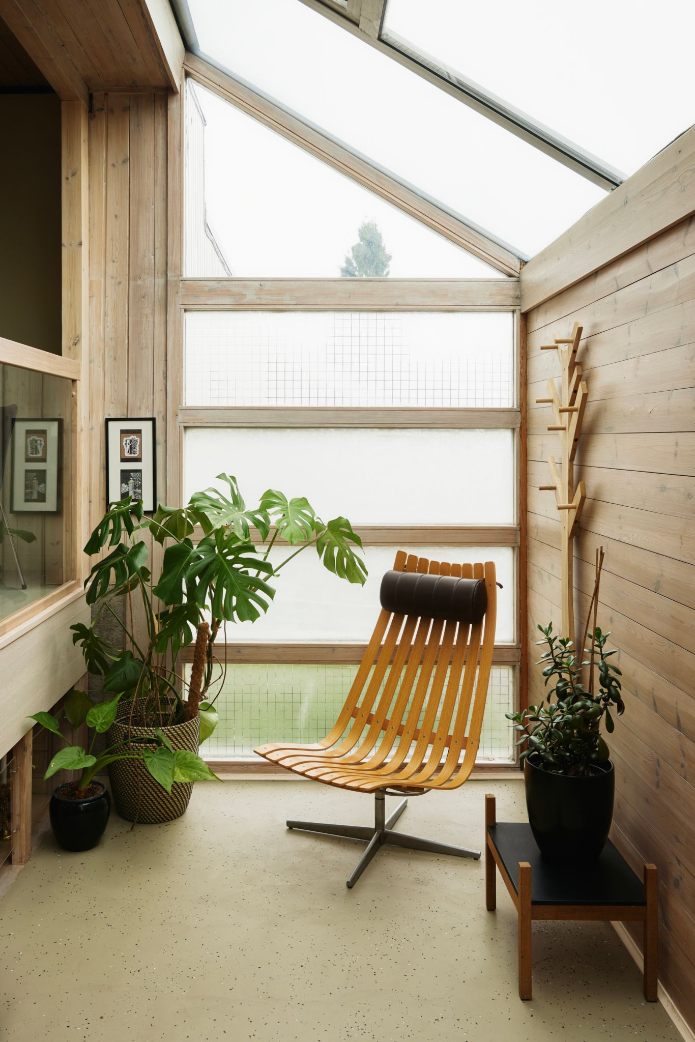 En stol står i et vindfang, veggene er dekket i panel og det er vindu i taket og på den ene veggen.