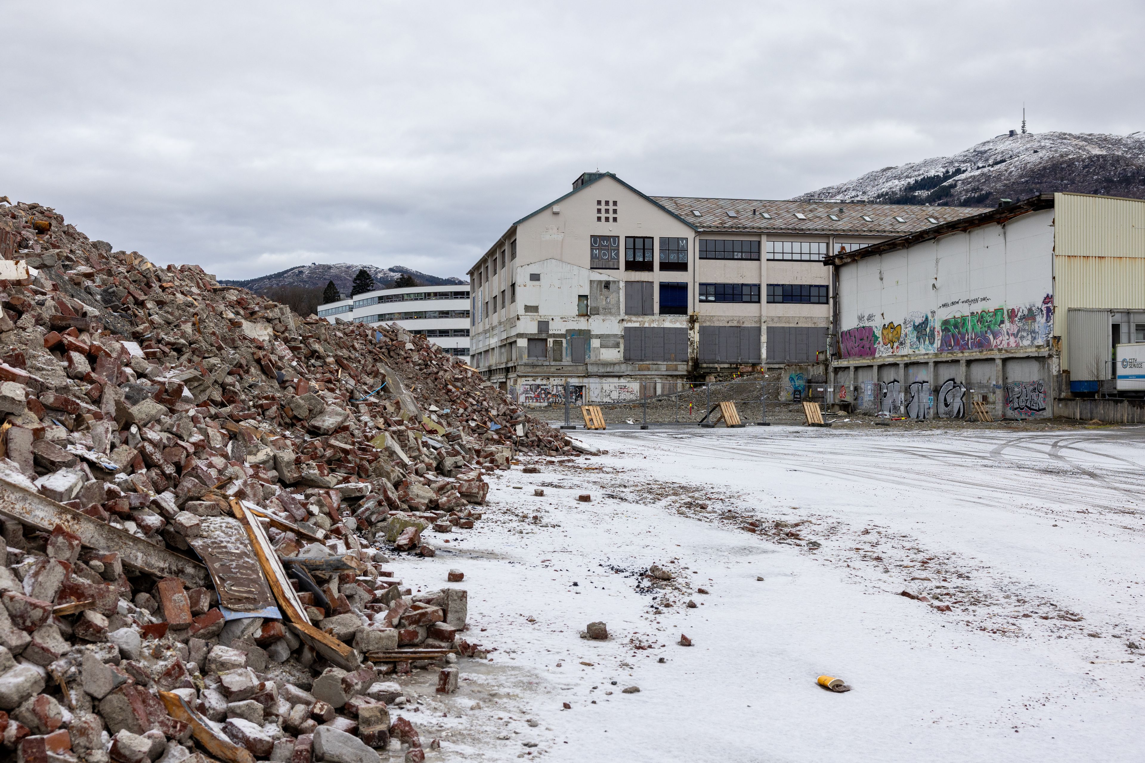 Bilde av den gamle tapperibygningen og en grushaug på byggetomten med Ulriken i bakgrunnen.