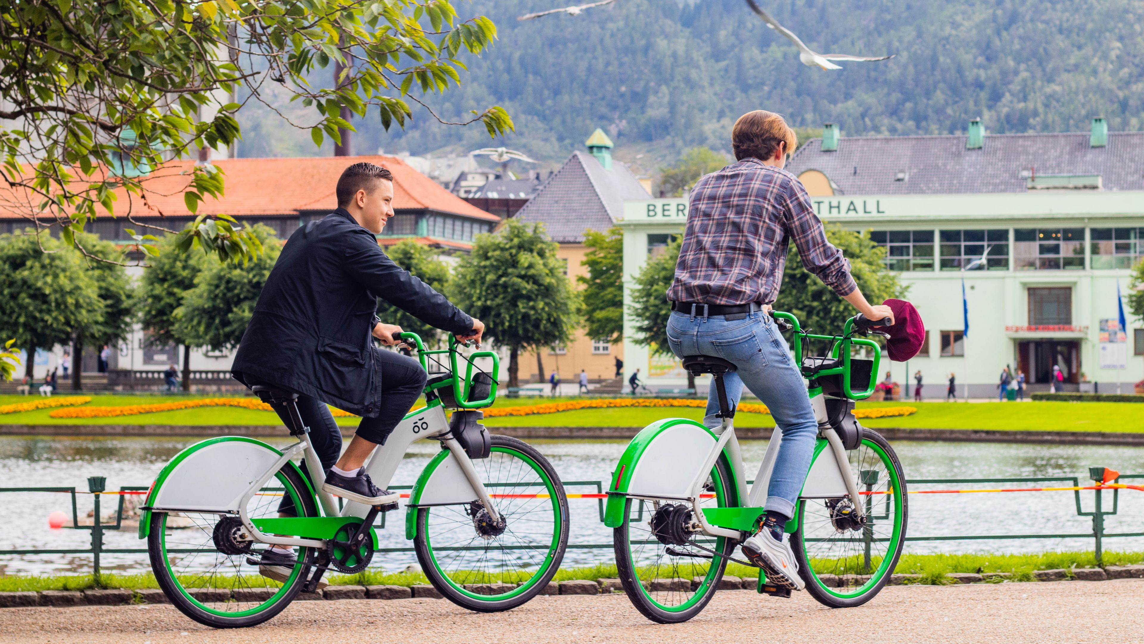 Foto av to gutter i Bergen sentrum som syker rundt på grønne bysykler.