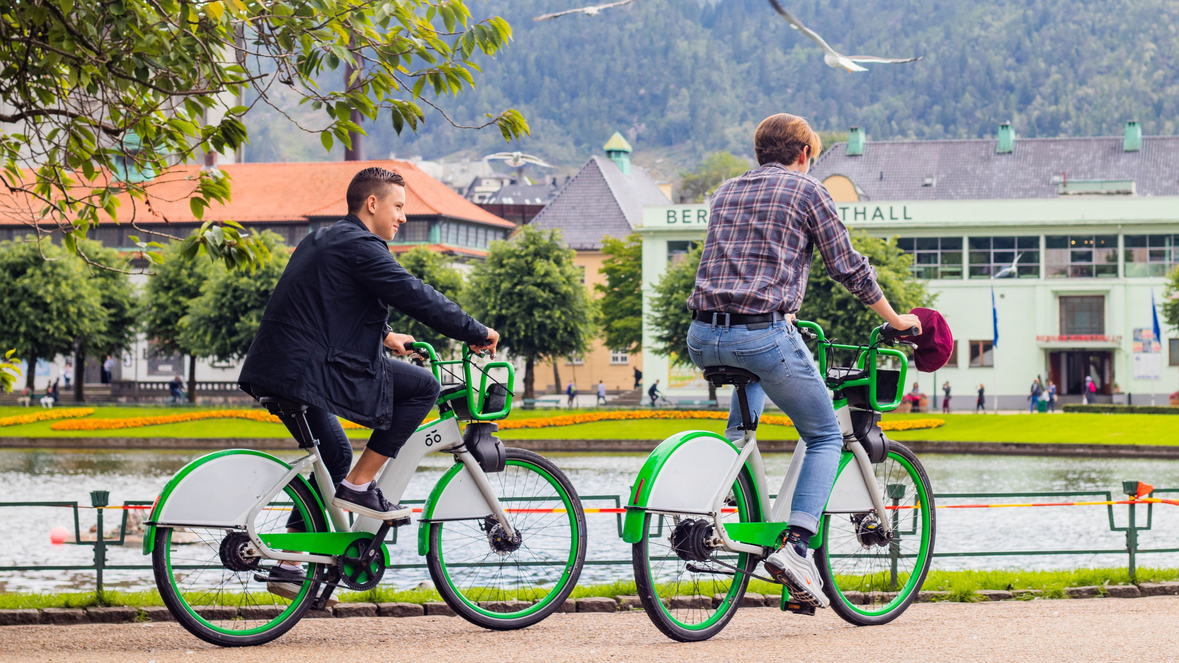 Foto av to gutter i Bergen sentrum som syker rundt på grønne bysykler.