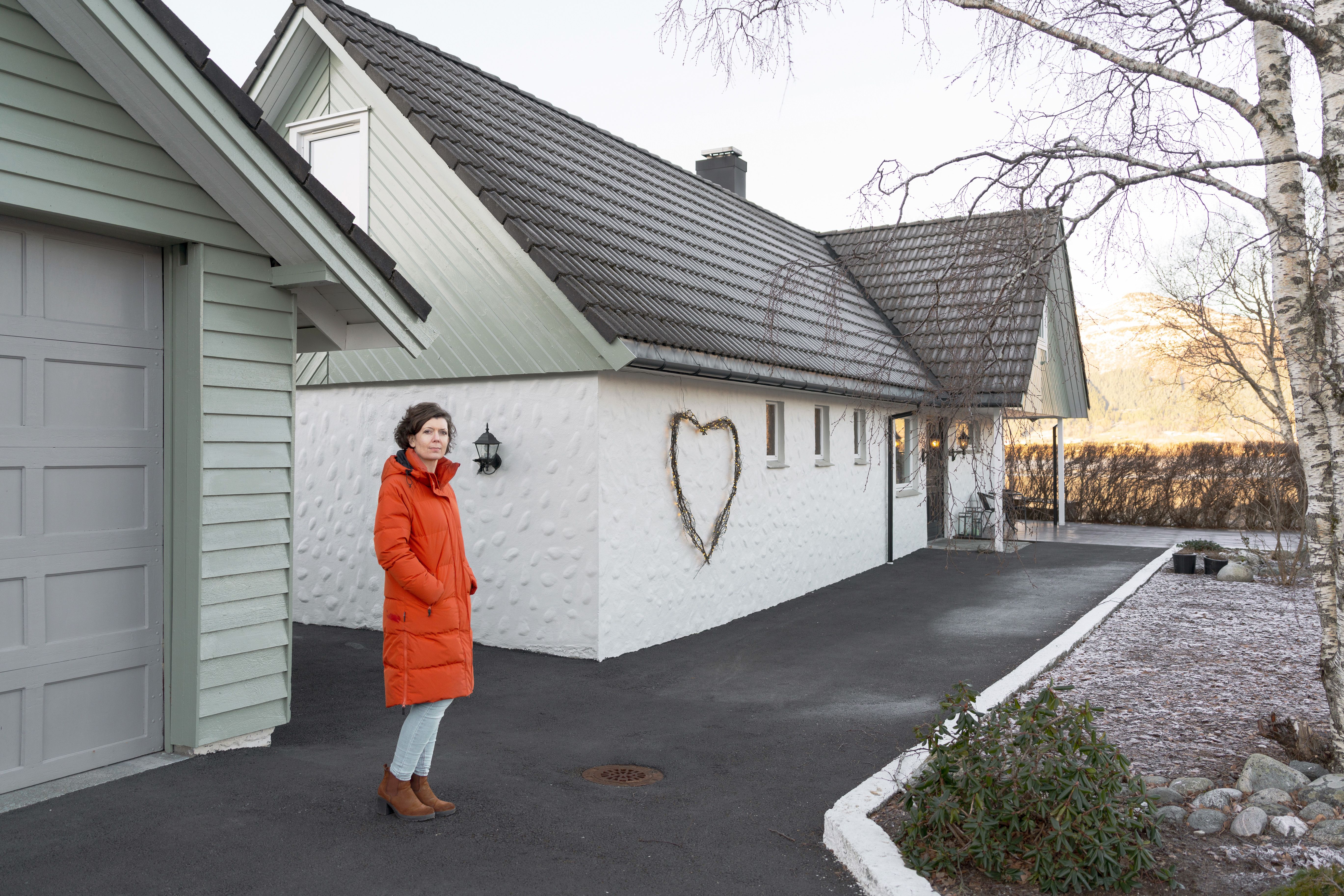 Marion Vik står utenfor eneboligen sin i Møre og Romsdal, iført lang, rød vinterjakke.