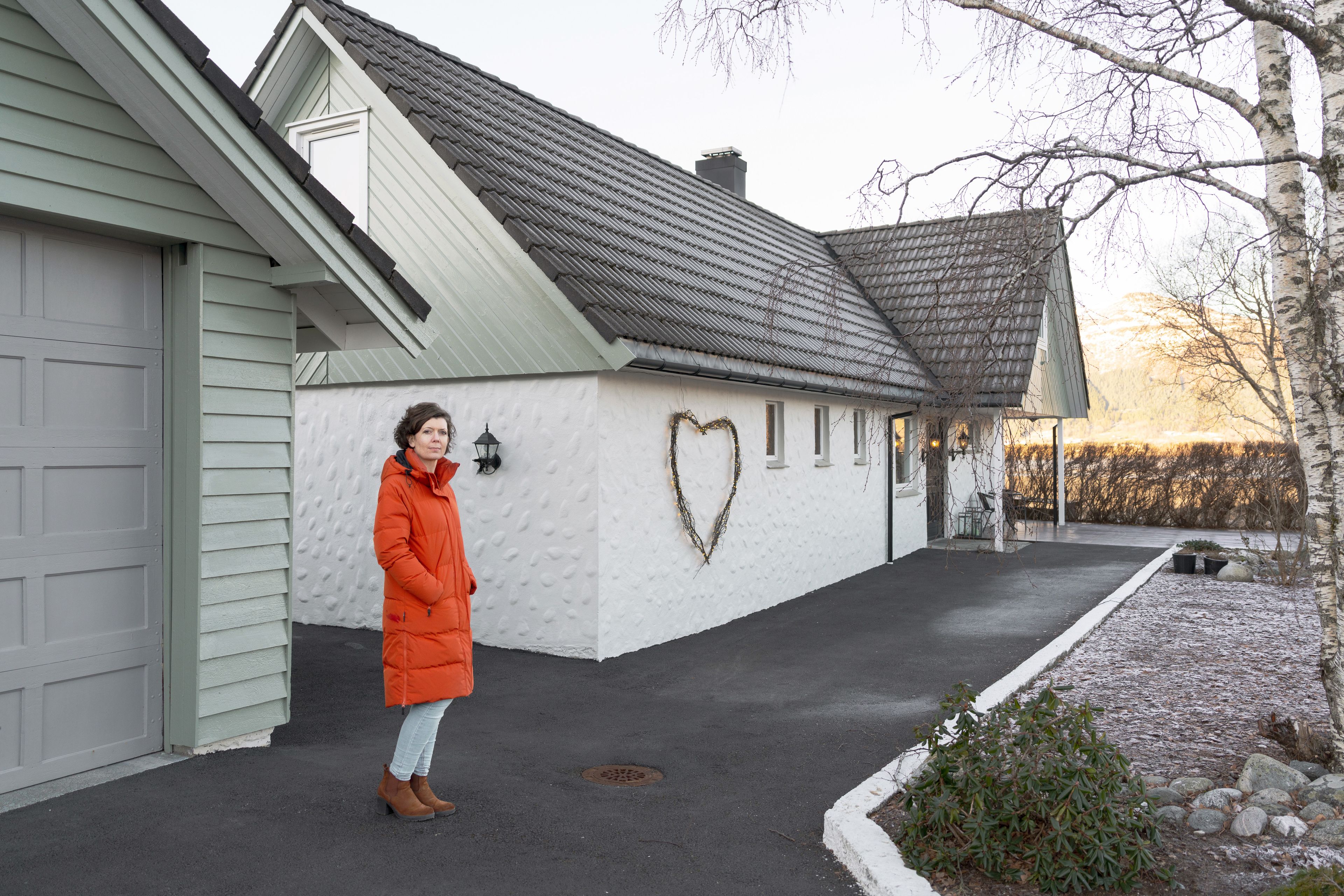 Marion Vik står utenfor eneboligen sin i Møre og Romsdal, iført lang, rød vinterjakke.