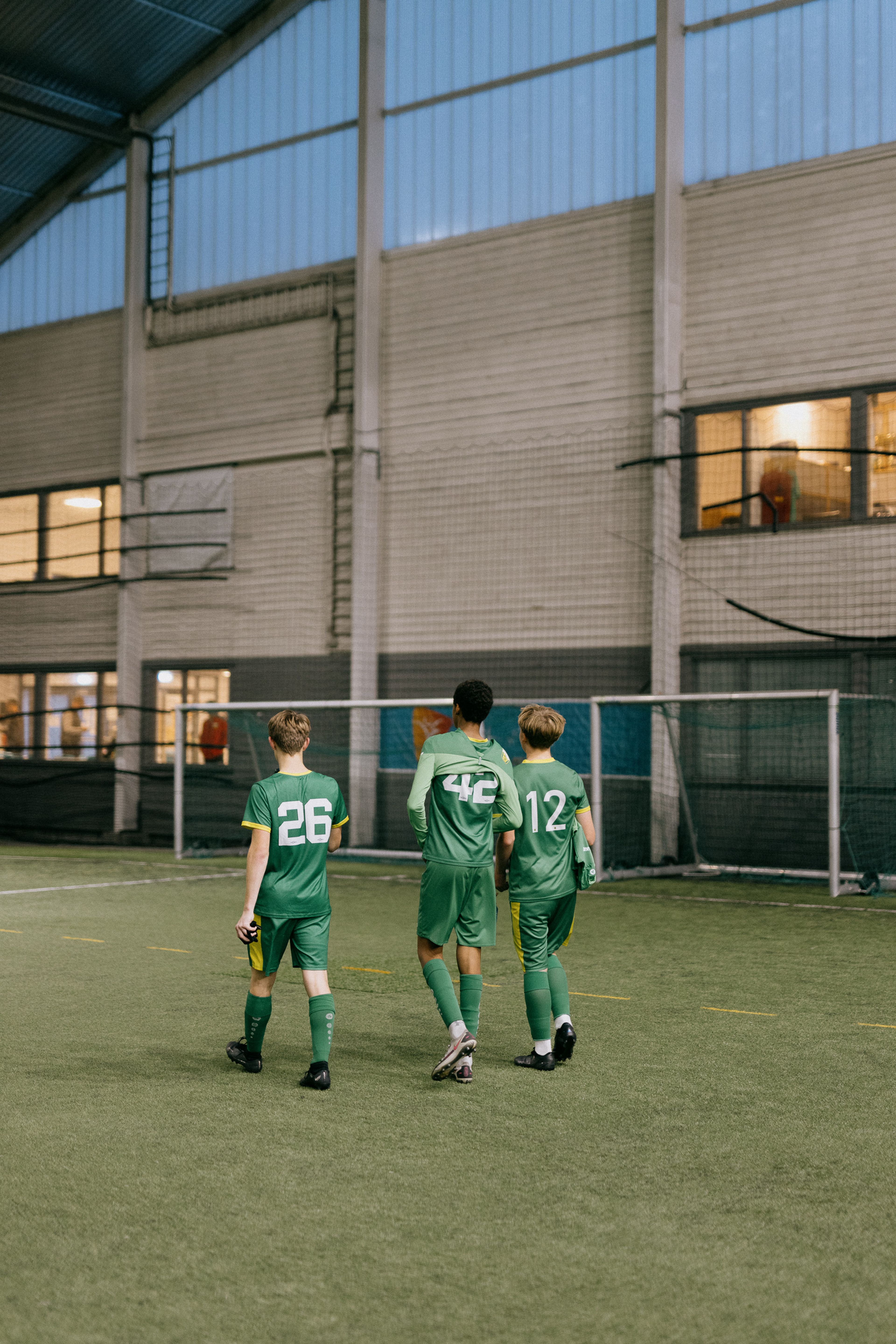 Tre gutter med grønne drakter går sammen inne i hallen.