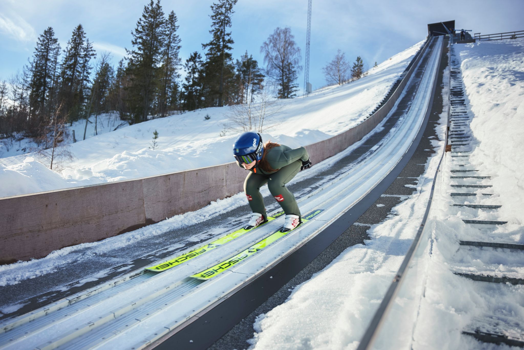 Jente forfra på vei ned ovarennet før et skihopp. Det er sol og klar himmel på bildet
