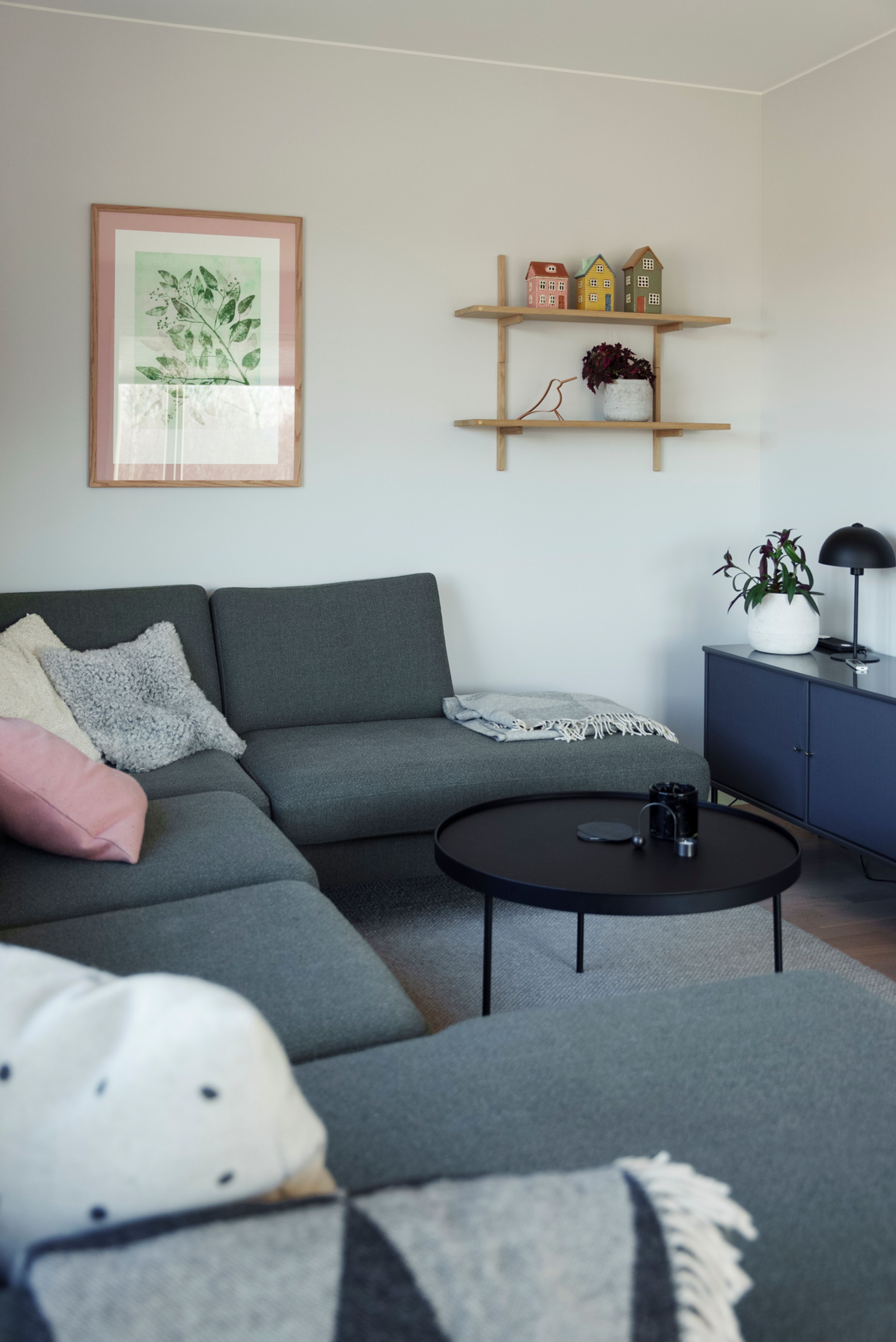 En gra sofa som omkranser et lite svart bord, mot en hvit vegg og en blå TV-benk