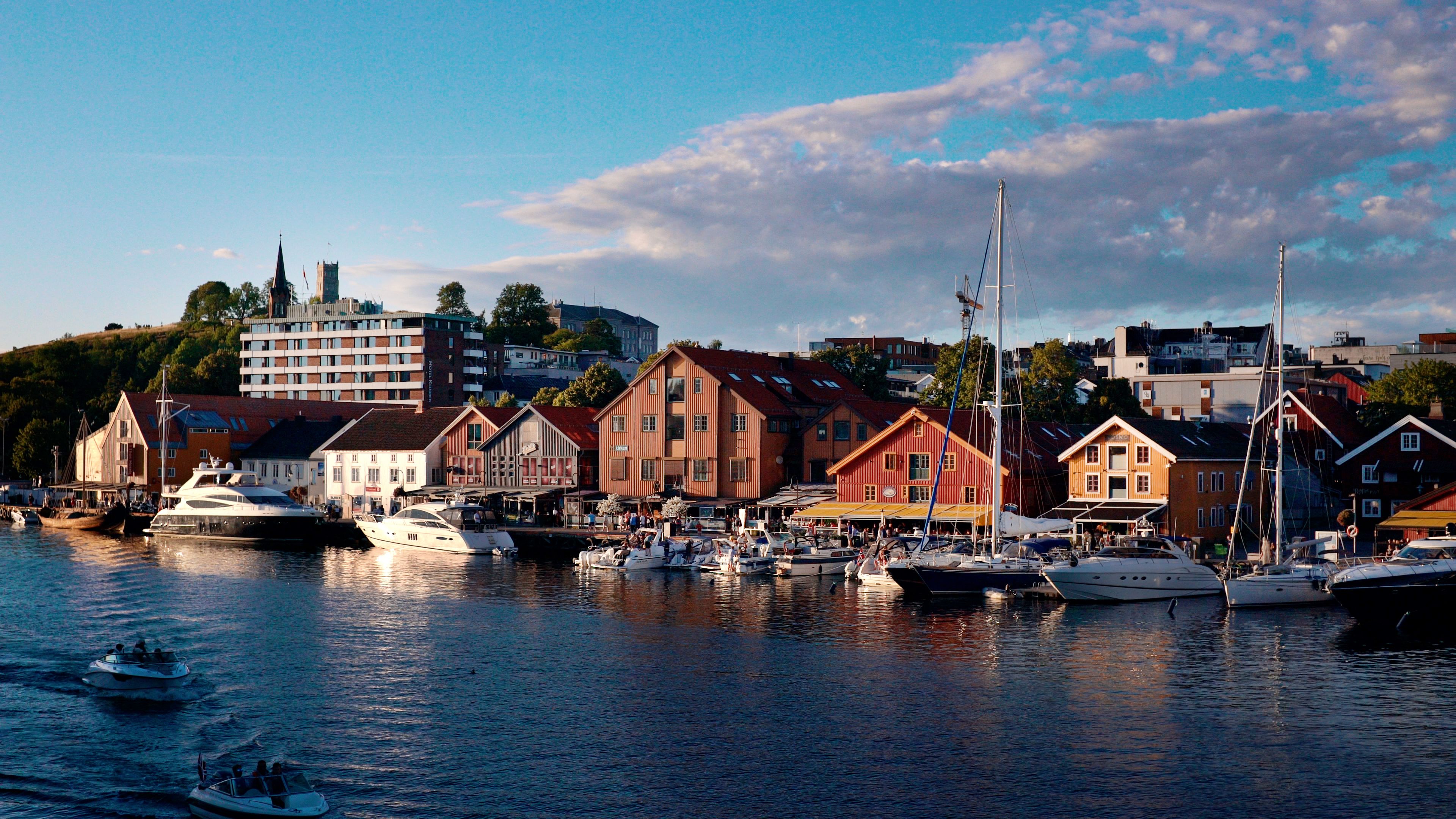 Tønsberg brygge i solnedgang, med røde og oransje bryggehus med restauranter og båter som ligger til kai.