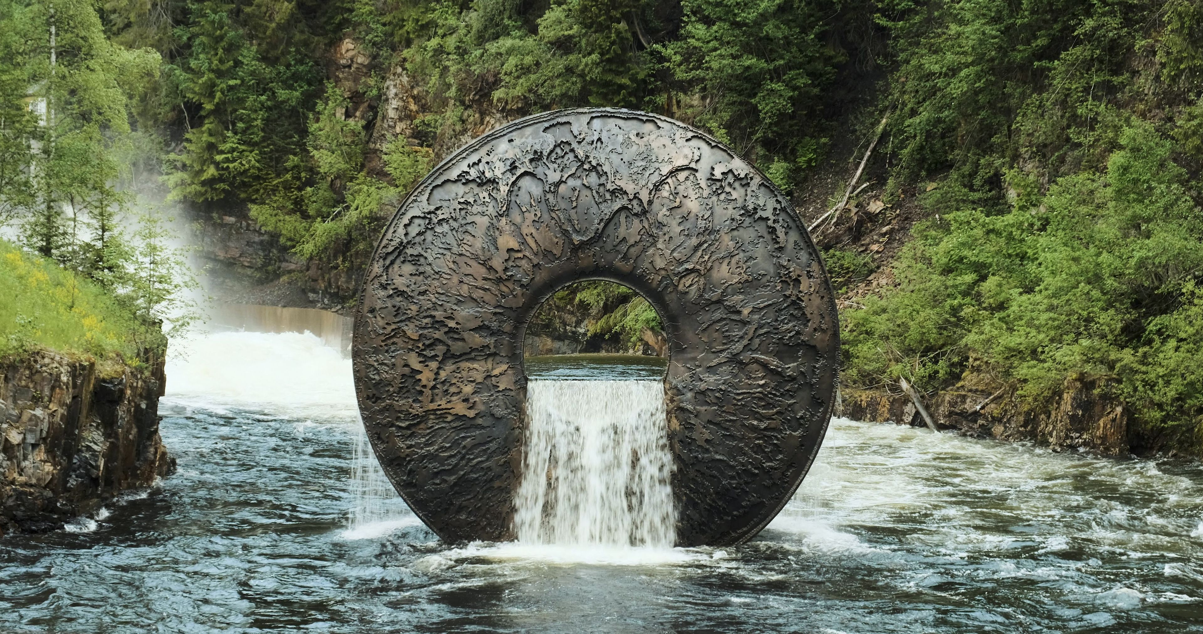 En steinskulptur i vannet. En foss renner gjennom et hull i steinen.