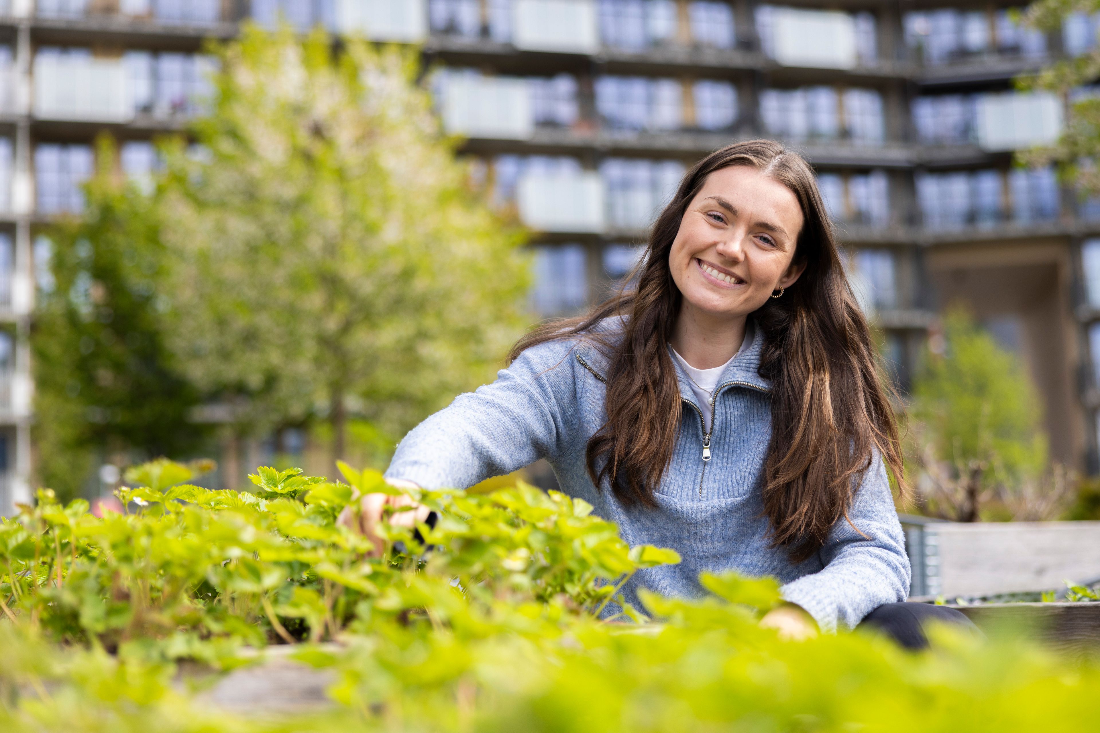 En smilende Johanne ved en plantekasse på Ulven.