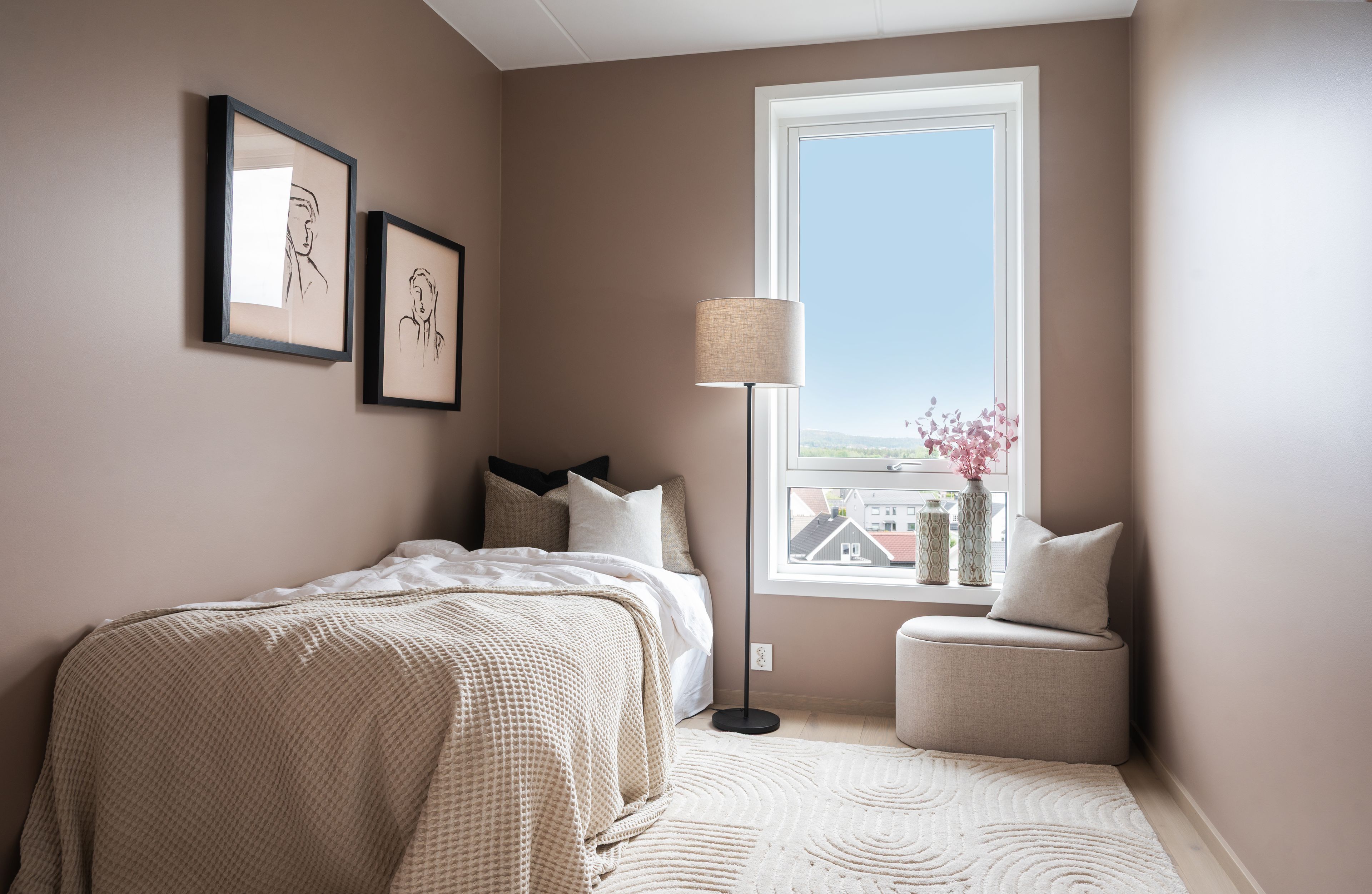 soverom med beige vegger, enkeltseng, stålampe og puff.