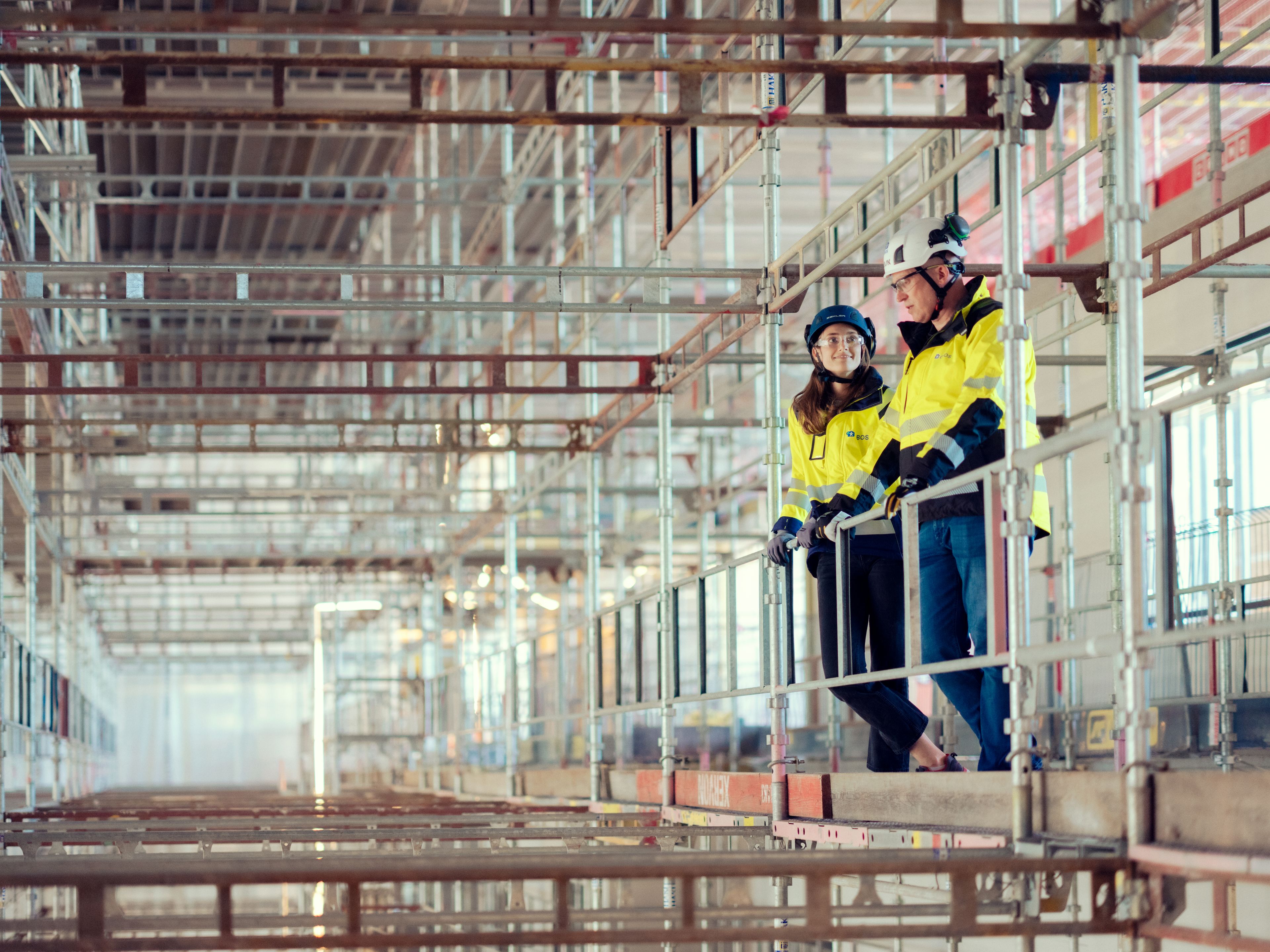 To byggearbeidere står i et stillas inne på en byggeplass.