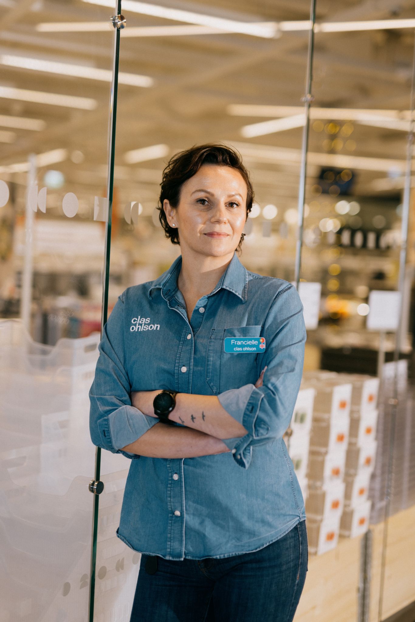 Foto av Francielle Lubke som har armene i korts mens hun smiler mot kameraet og lener seg mot glassveggen til Clas Ohlson butikken.