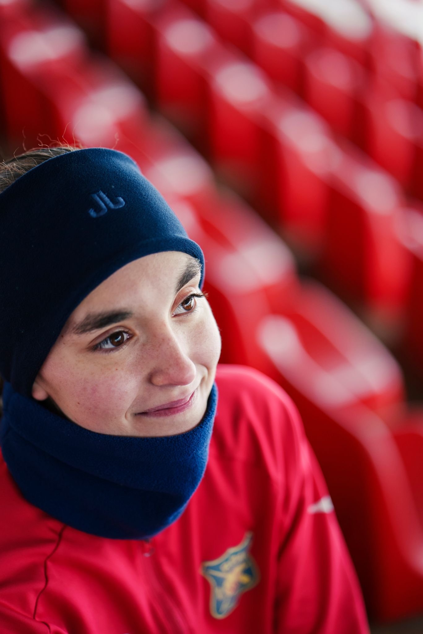 Et nærbilde av Sara som sitter på tribunen. Hun har på seg rød drakt og svart pannebånd.